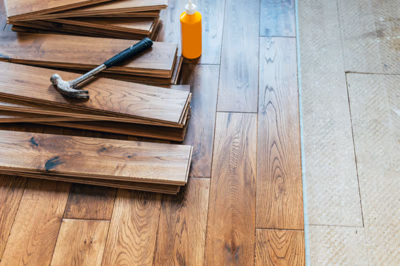 A partially finished wood plank floor with extra planks piled up