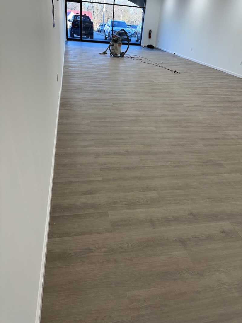 Newly installed wide-plank luxury vinyl flooring running the length of a commercial retail space in Lebanon, NJ, with storefront glass at the far end