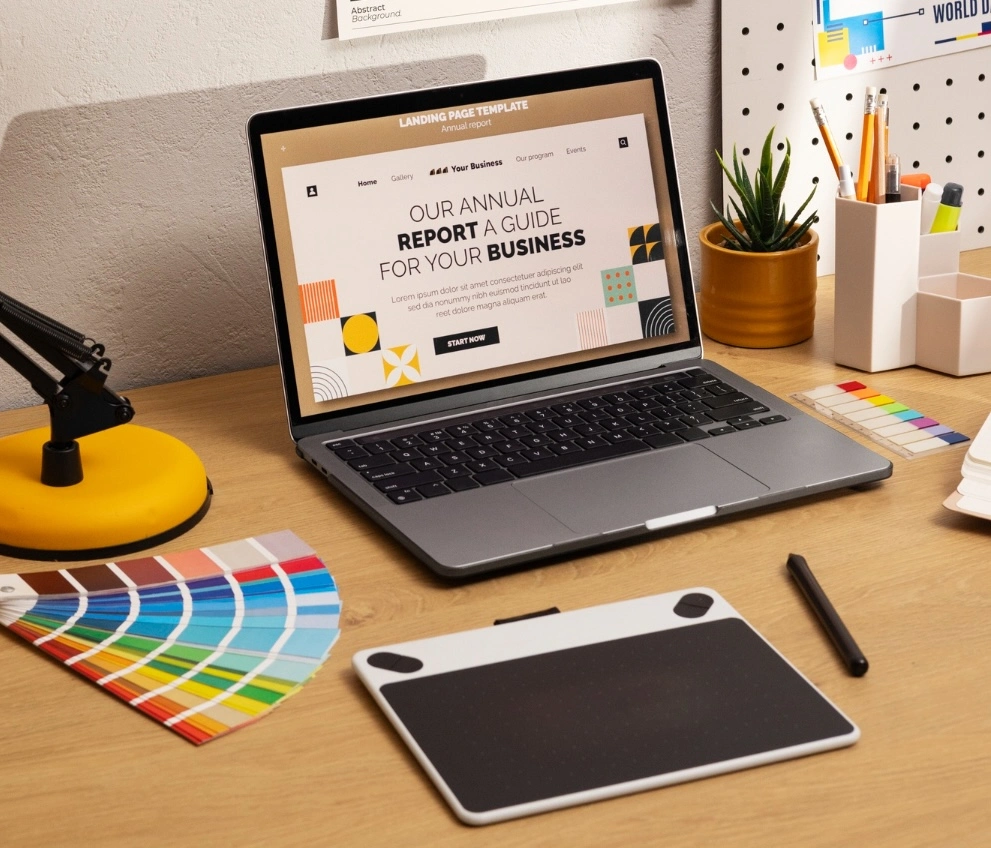 Workspace with a laptop displaying a business report, color swatches, a graphics tablet, and office supplies on a wooden desk.