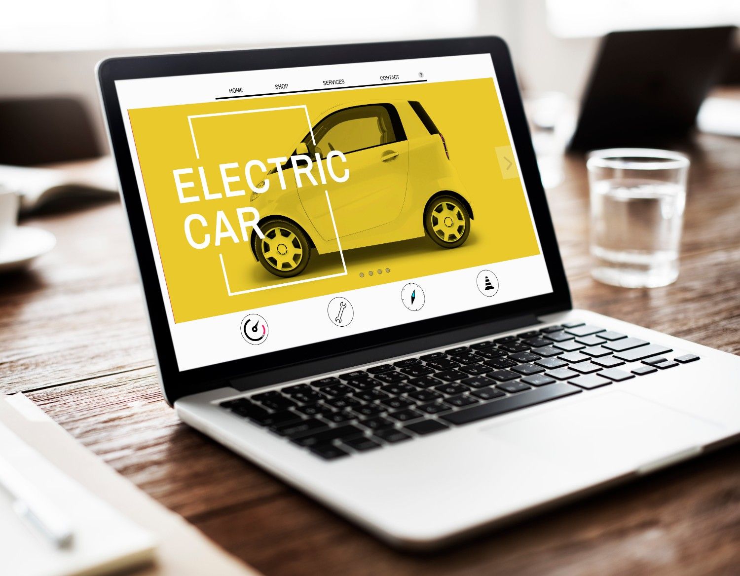 Laptop on a wooden table displaying a webpage about electric cars, featuring a bright yellow car and the text 'ELECTRIC CAR' on screen.