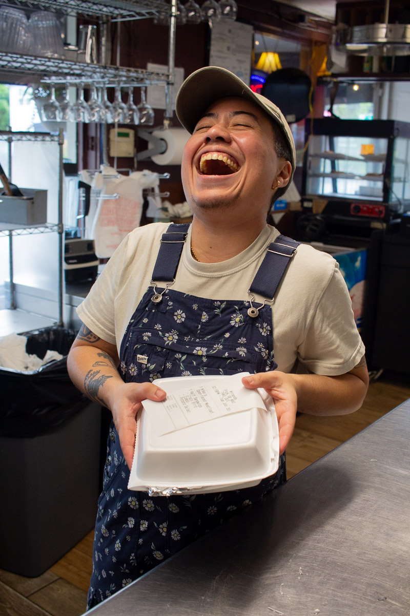 A 903 Mills Market employee laughing while holding a delivery meal.