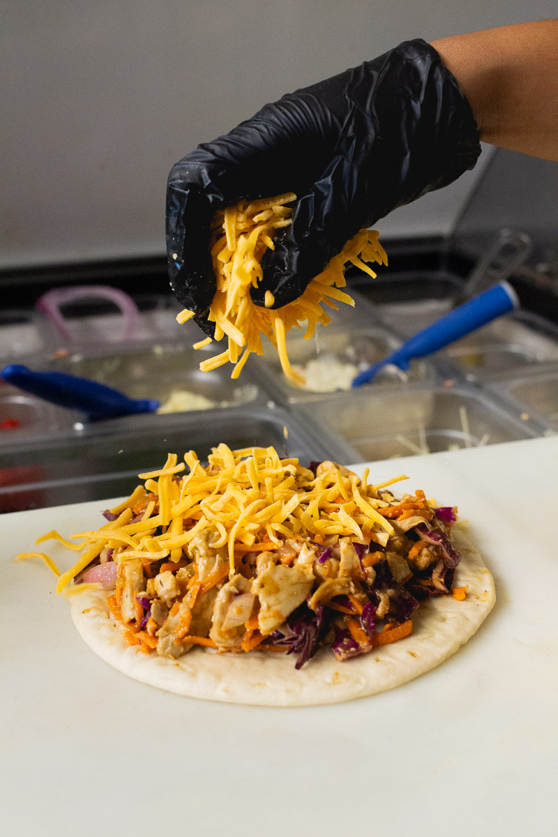 A hand sprinkling cheese over a sandwich wrap.