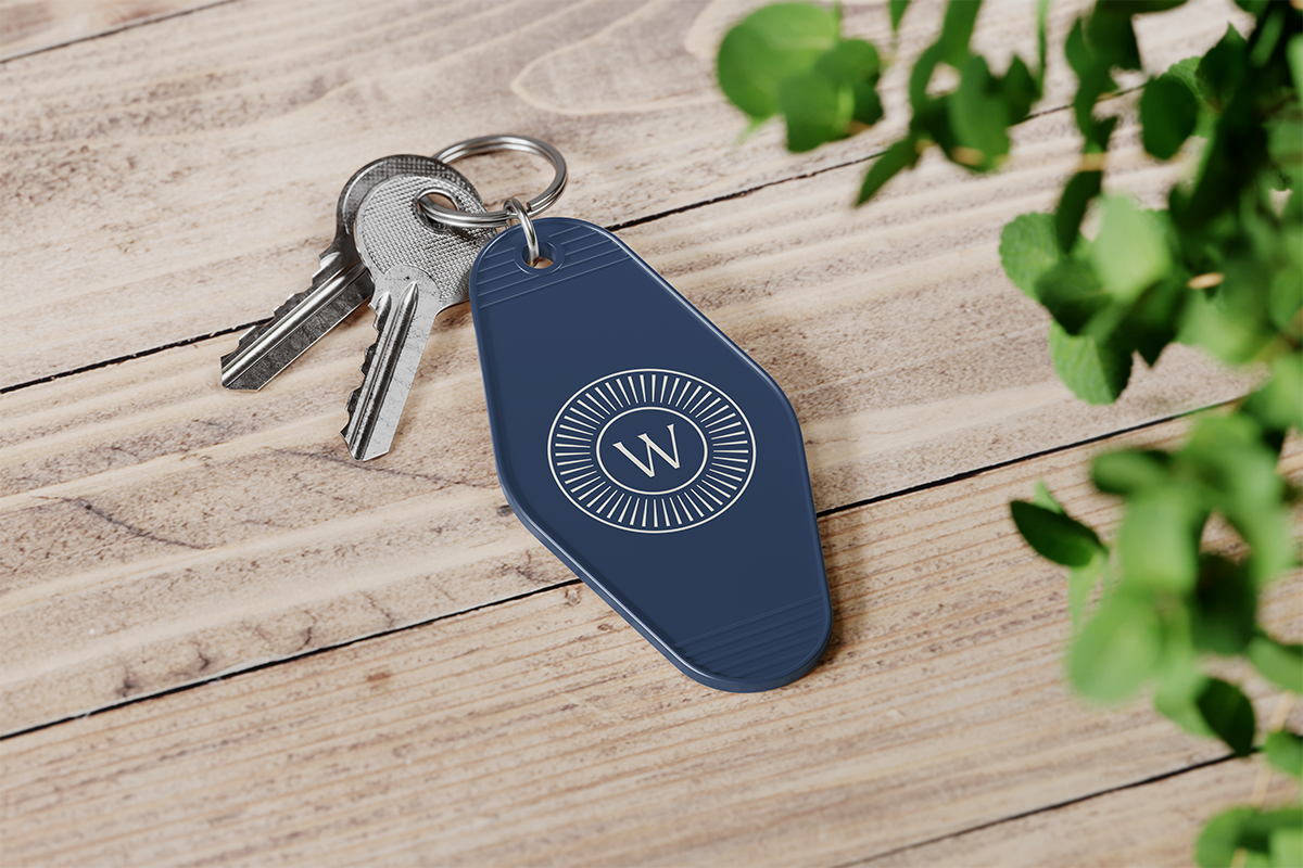 A photo of a branded The Welcome Standard keychain on wooden desk.