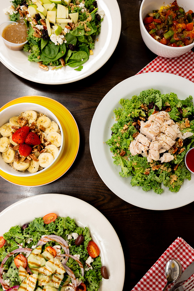 Overhead shot of 3 salads and oatmeal bowl on a wooden table.