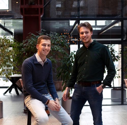 Twee jonge professionals glimlachen in een moderne, groene kantooromgeving