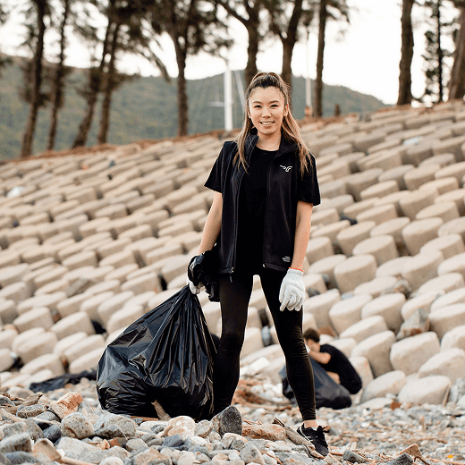 A woman holding rubbish bags outside in front of palm trees