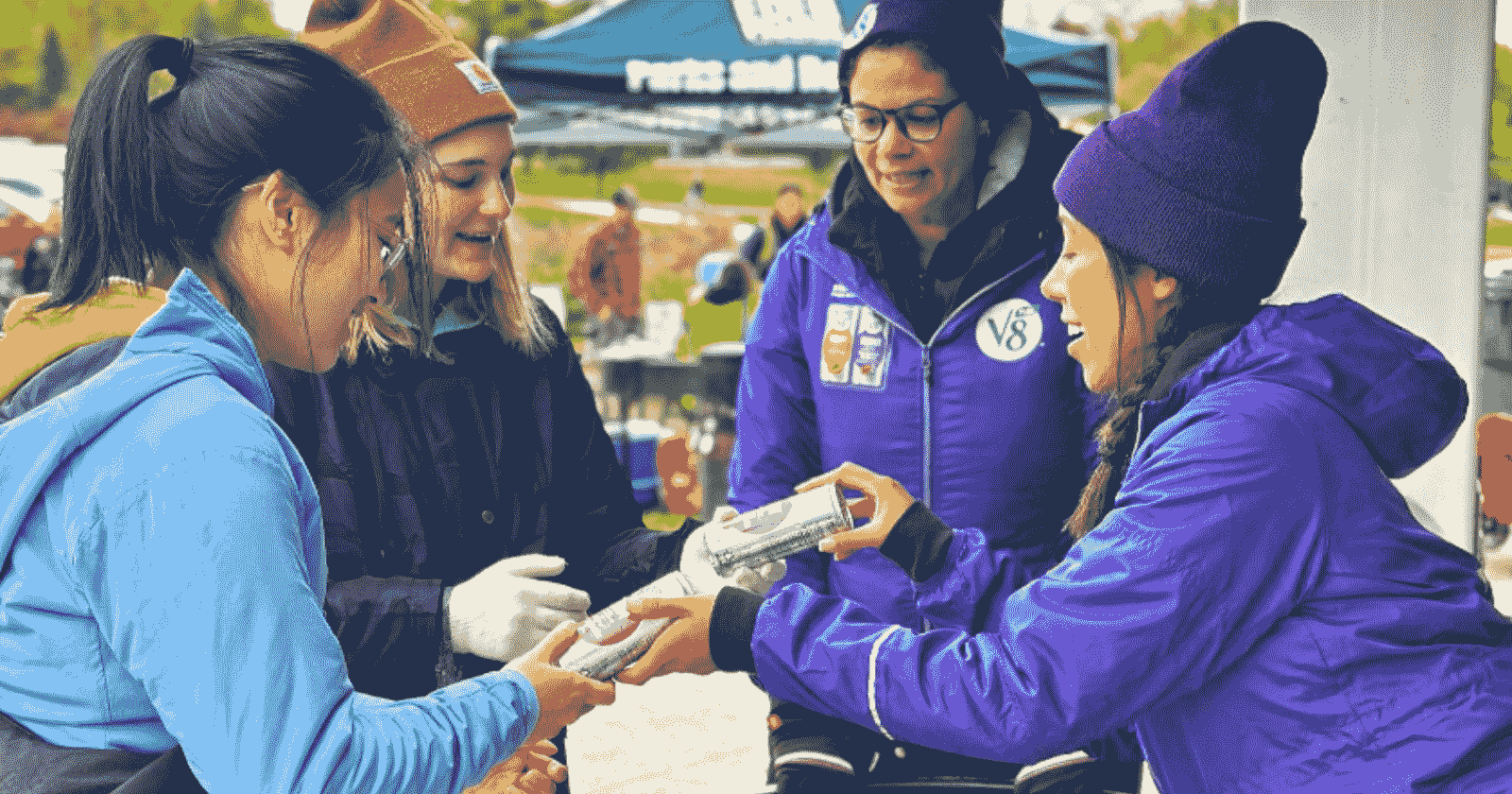 woman giving out V8 to two woman