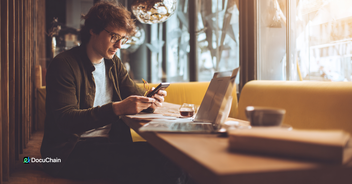Man reviews signing workflow on phone and laptop in café, illustrating how DocuChain supports flexible remote eSign setup