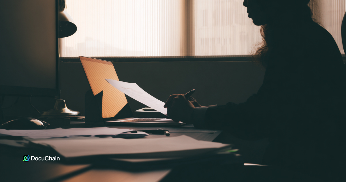Silhouetted worker holds printed contract in dark office, symbolizing time and money lost to paper-based processes