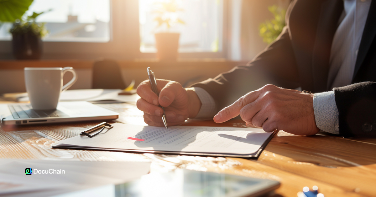 Close-up of hand signing paper document, contrasting with laptop on desk — highlighting the switch to paperless signing with DocuChain