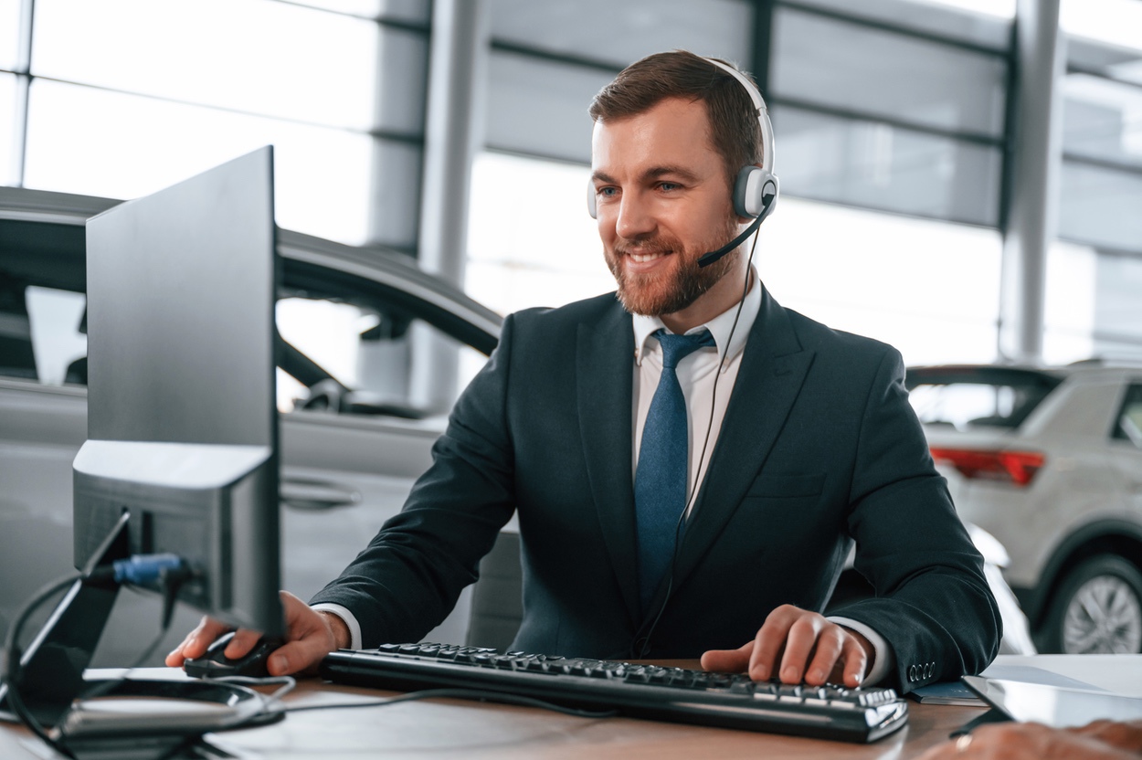 Auto sales representative placing call via headset to prospective customer from showroom floor in dealership