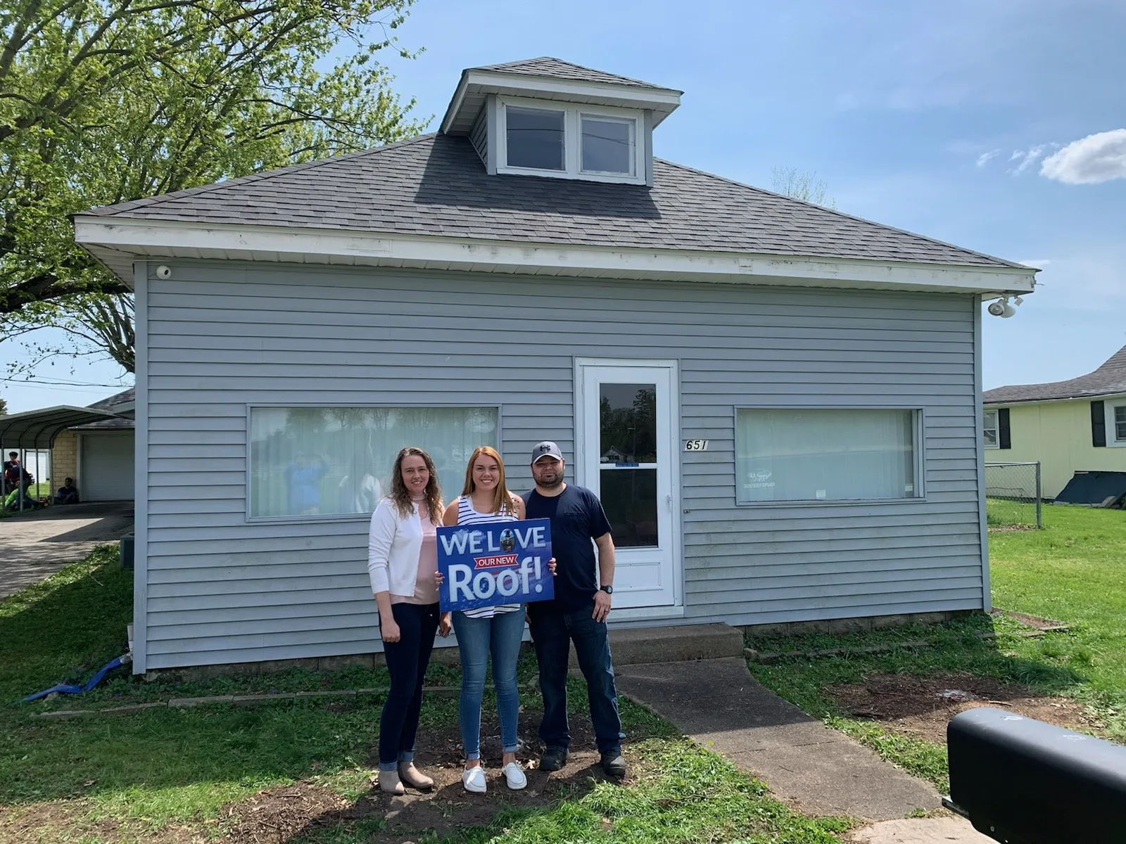 Honest Abe Roofing customers outside their home with a We Love Our New Roof sign