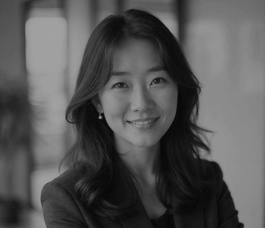 A black and white portrait of a smiling Asian woman with long wavy hair, wearing a blazer.