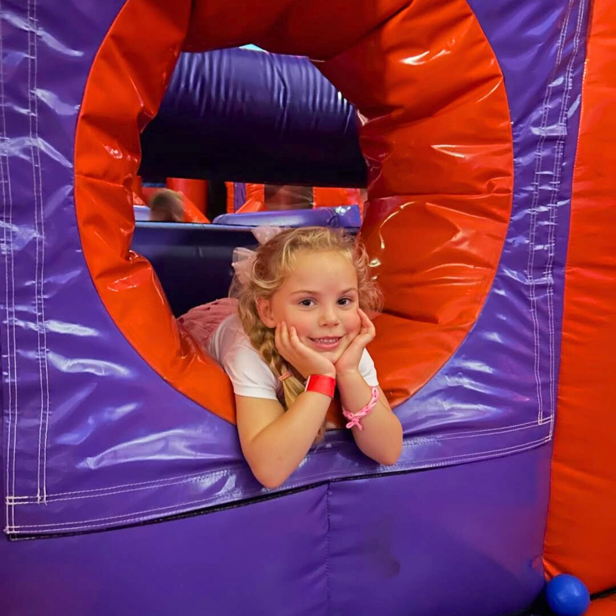 Child smiling through a circular obstacle at an inflatable park.