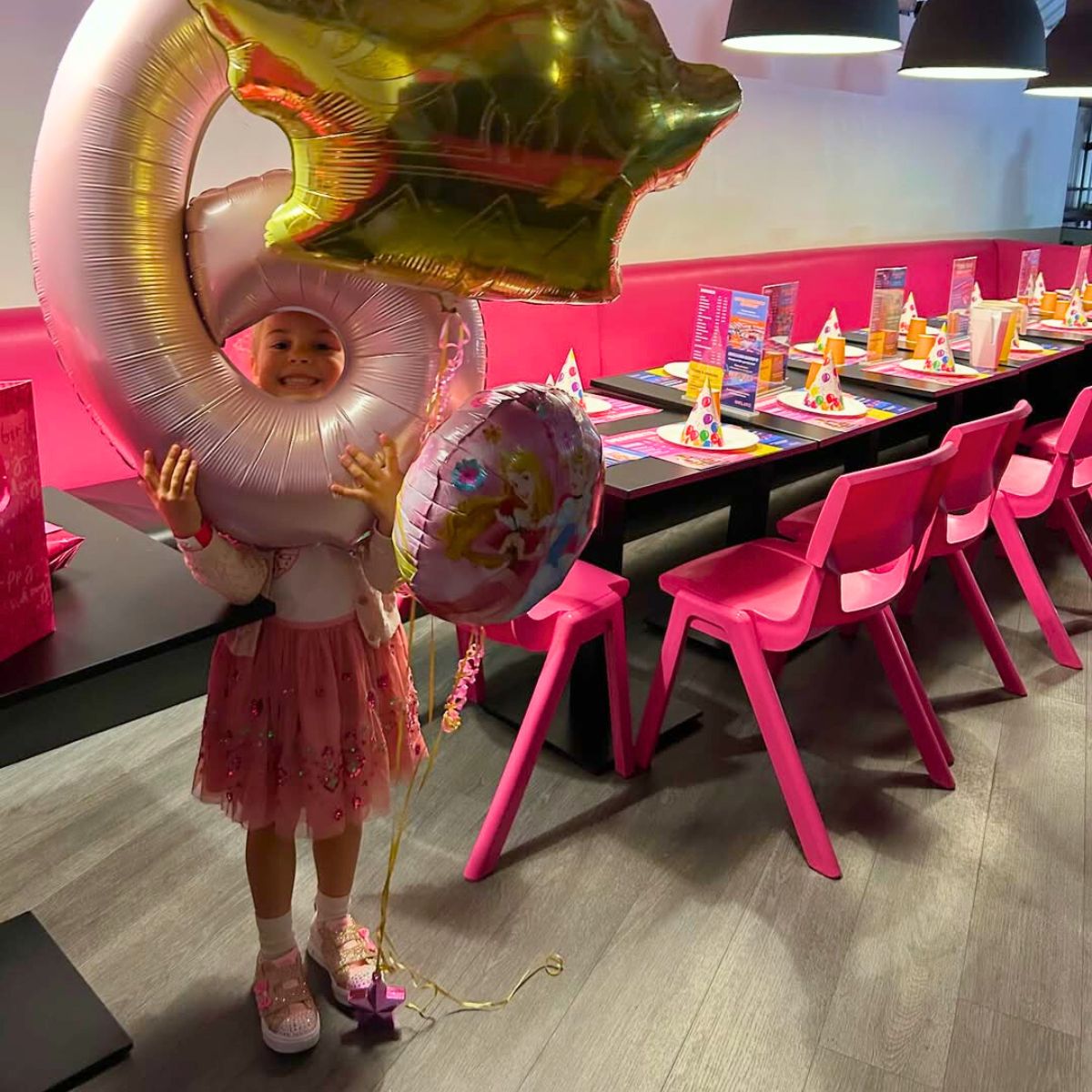 Child holding large birthday balloons in a bright party area.