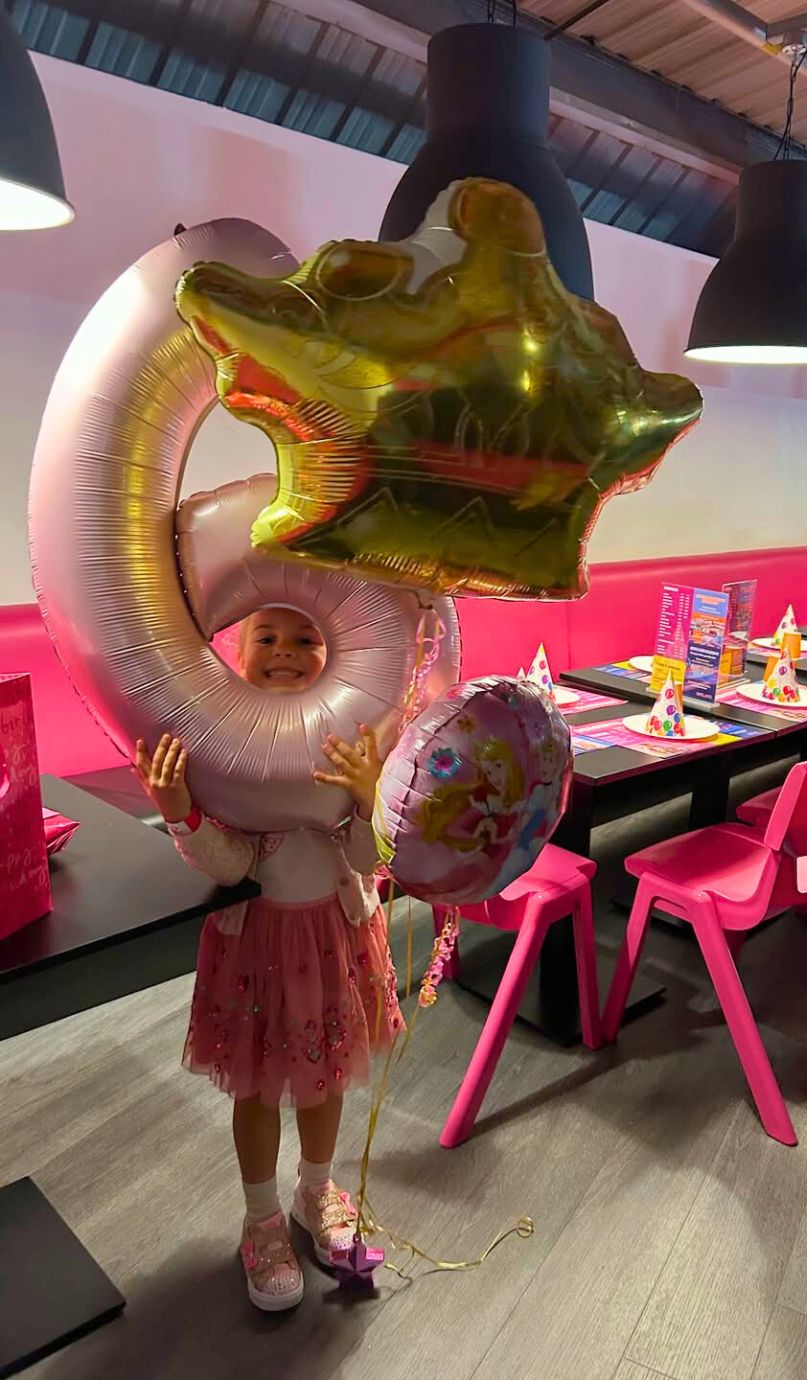 Child holding large birthday balloons in a bright party area.
