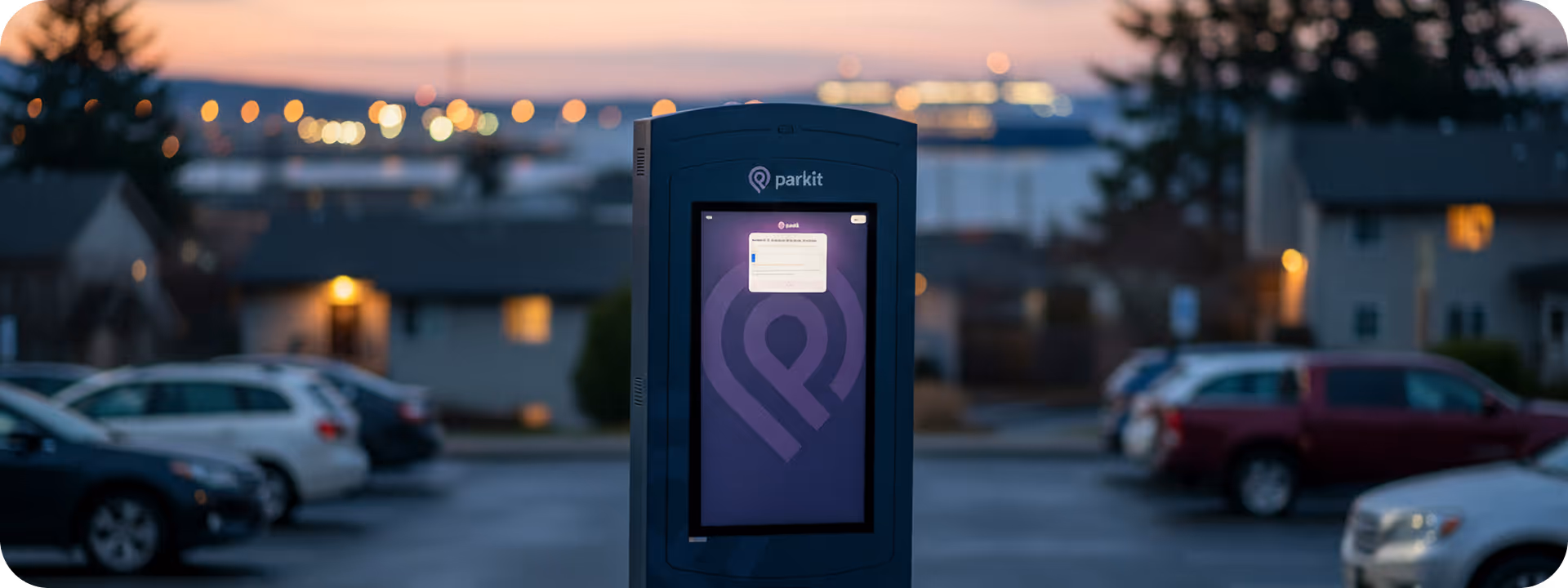 Betalningsautomat för parkering med digital skärm i parkeringsområde vid skymning.