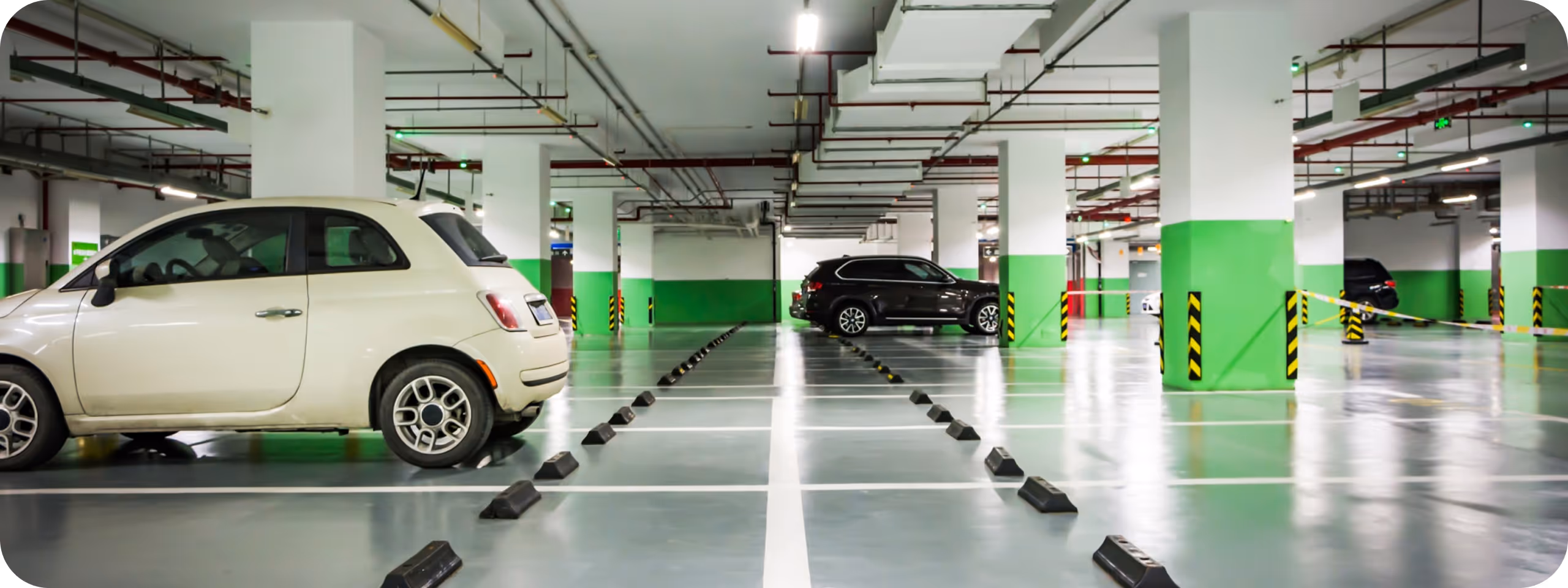 Underjordiskt parkeringsgarage med vita och svarta bilar parkerade mellan gröna och vita pelare.