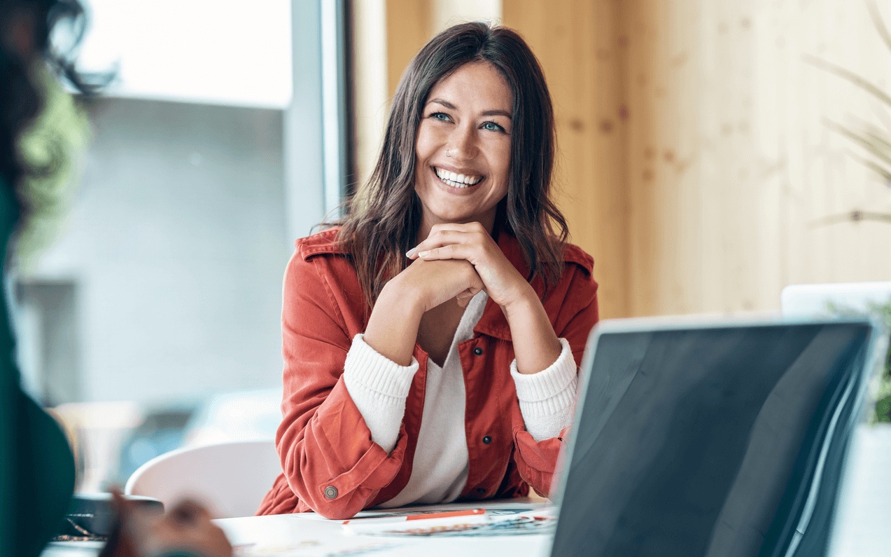 Smiling woman sitting confidently at her work desk, talking to a colleague, after cosmetic dental procedures and the best smile makeover in Los Gatos, CA.