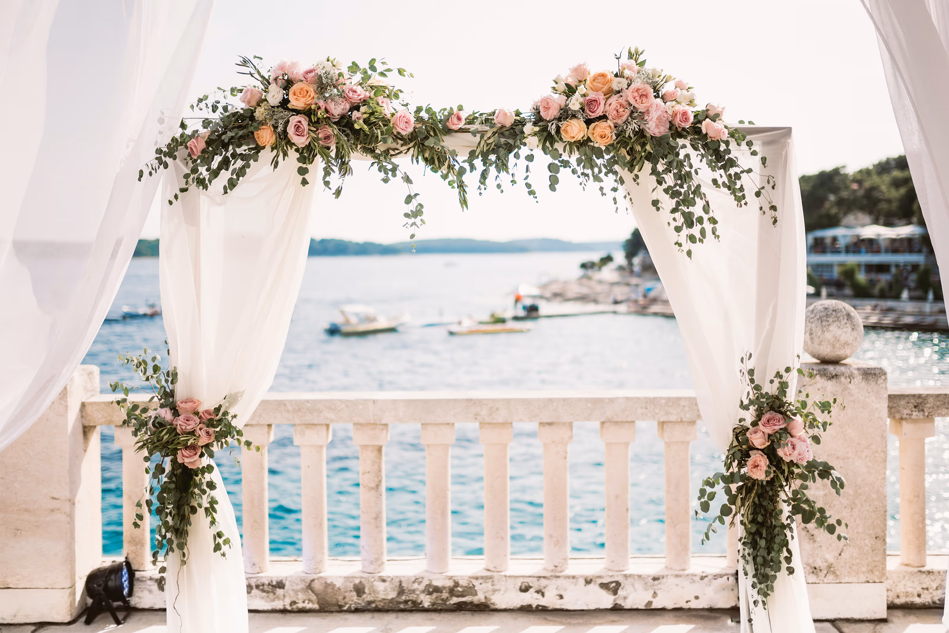 Wedding arch decorated with pink and peach roses and greenery overlooking a waterfront with boats at an all-inclusive Dominican Republic wedding resort.