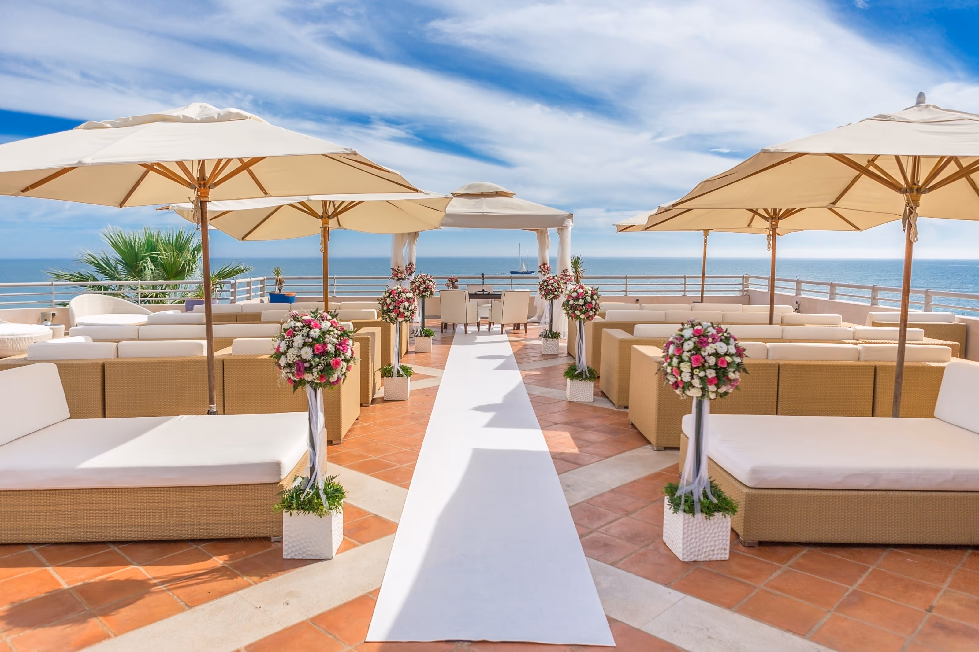 Outdoor Dominican Republic destination wedding ceremony setup with white aisle runner, floral arrangements, seating, and umbrellas by the ocean.