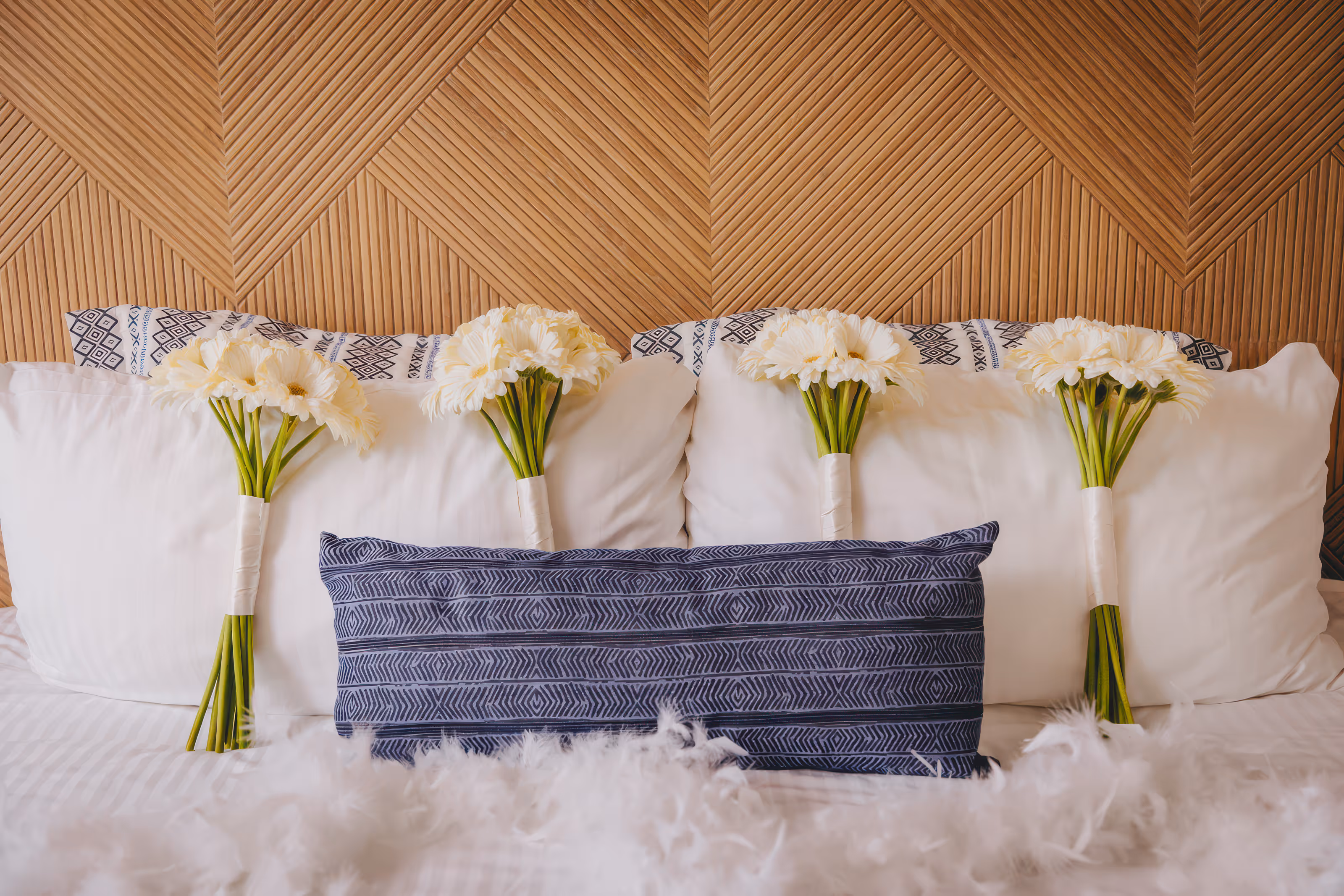 Four bouquets of white flowers on a bed with white and patterned pillows and a blue cushion at an all-inclusive Dominican Republic wedding resort.