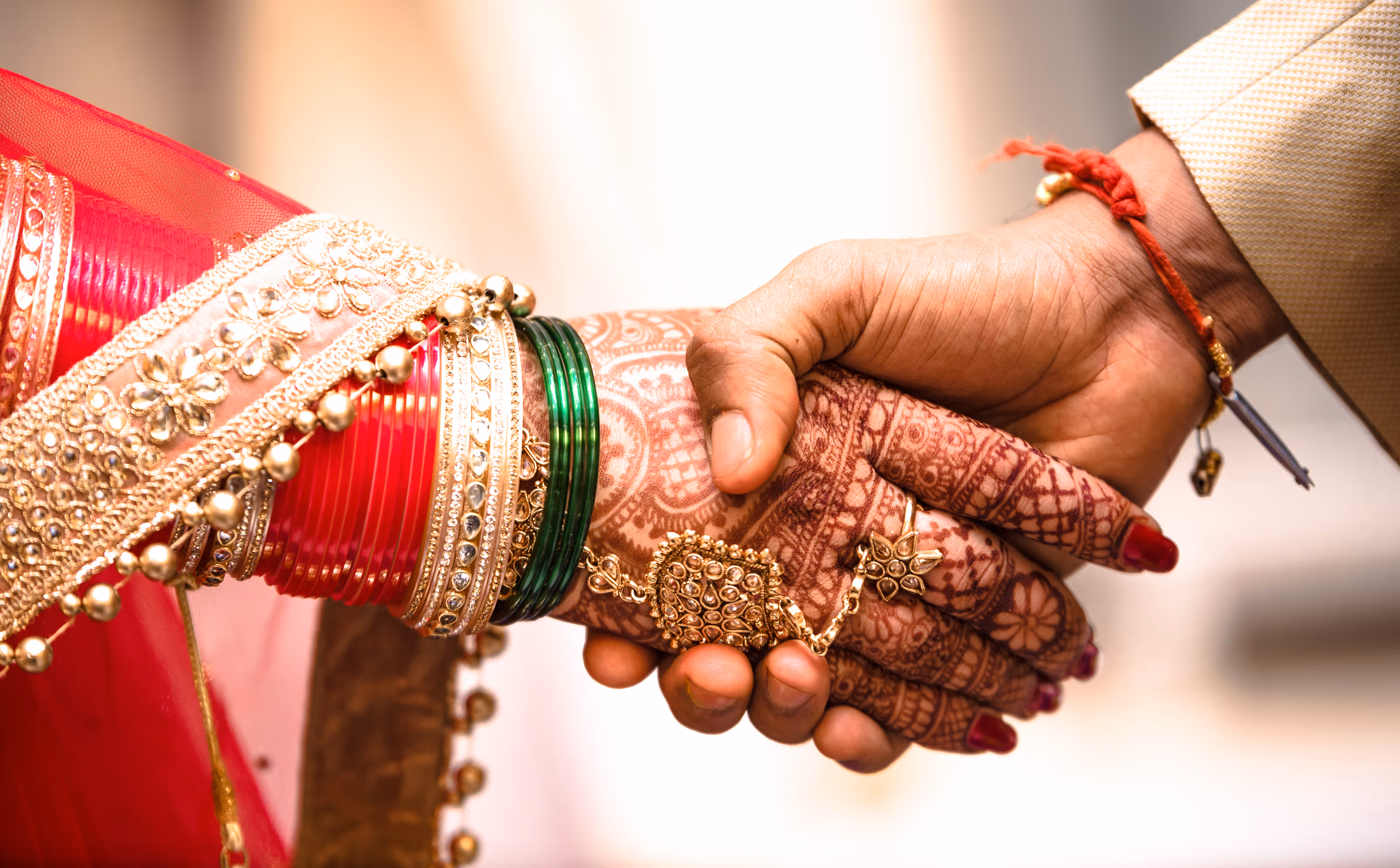 Close-up of two hands holding, one adorned with mehndi, bangles, and jewelry in traditional attire for a South Asian destination wedding.