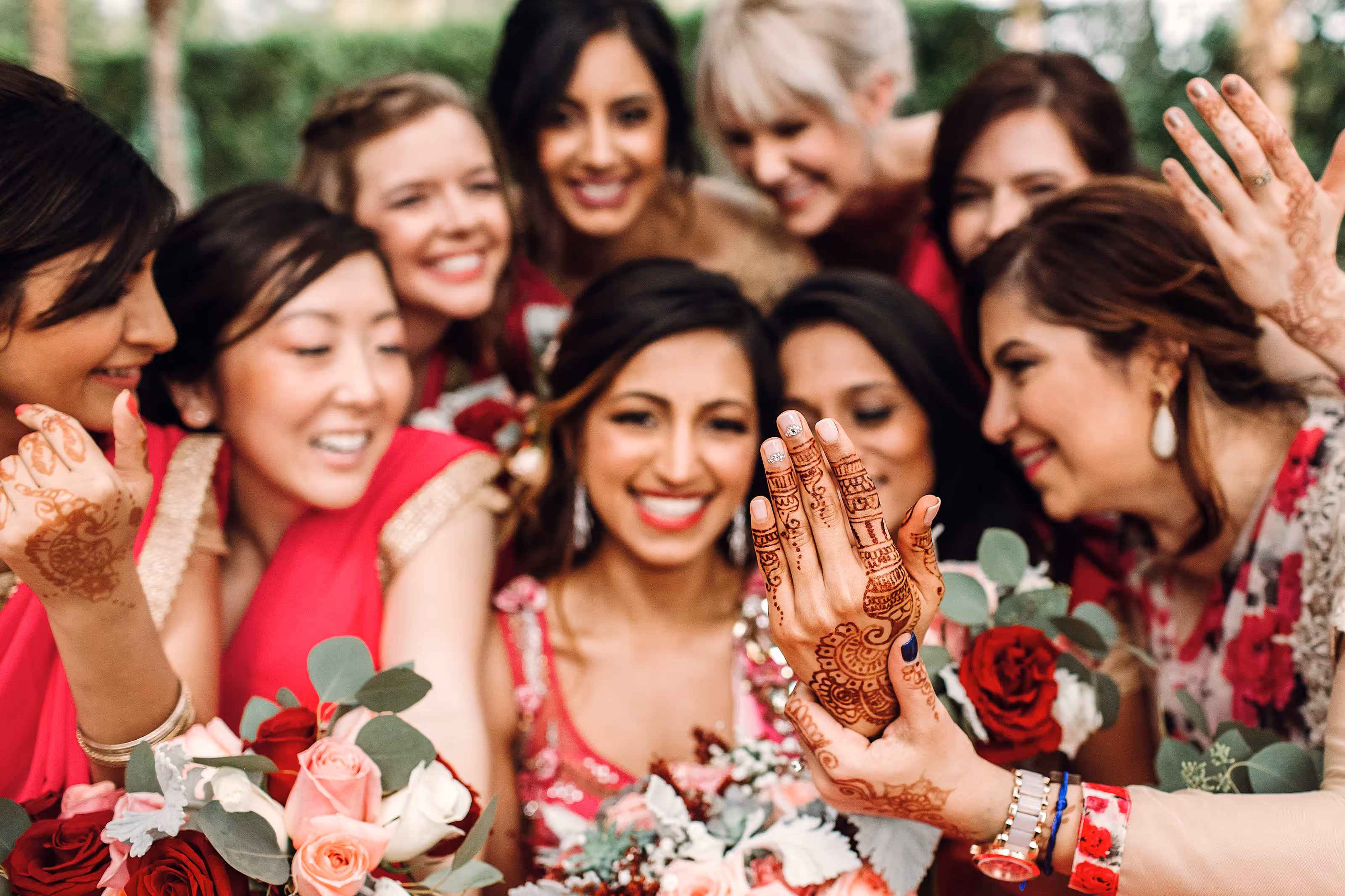 Smiling bride and friends showing intricate henna designs on hands and holding flower bouquets at a South Asian destination wedding.