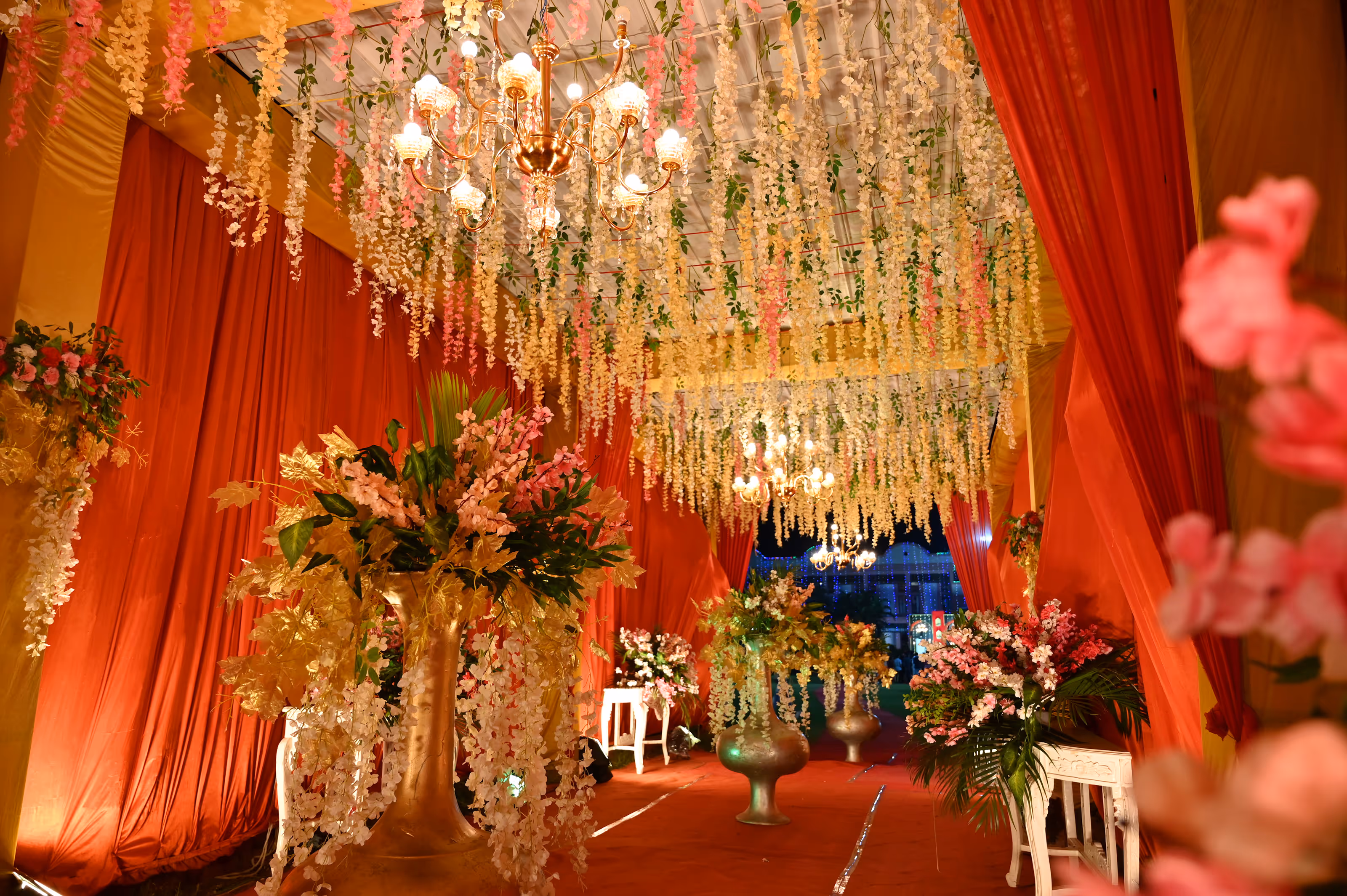 Decorated all-inclusive wedding resort venue with hanging white and pink flowers, chandeliers, and large floral arrangements in golden vases.