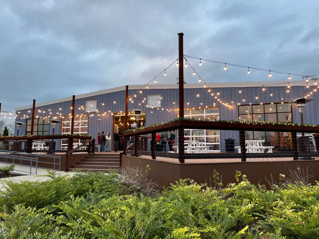 Guests at high-top tables in a brewery taproom under string lights