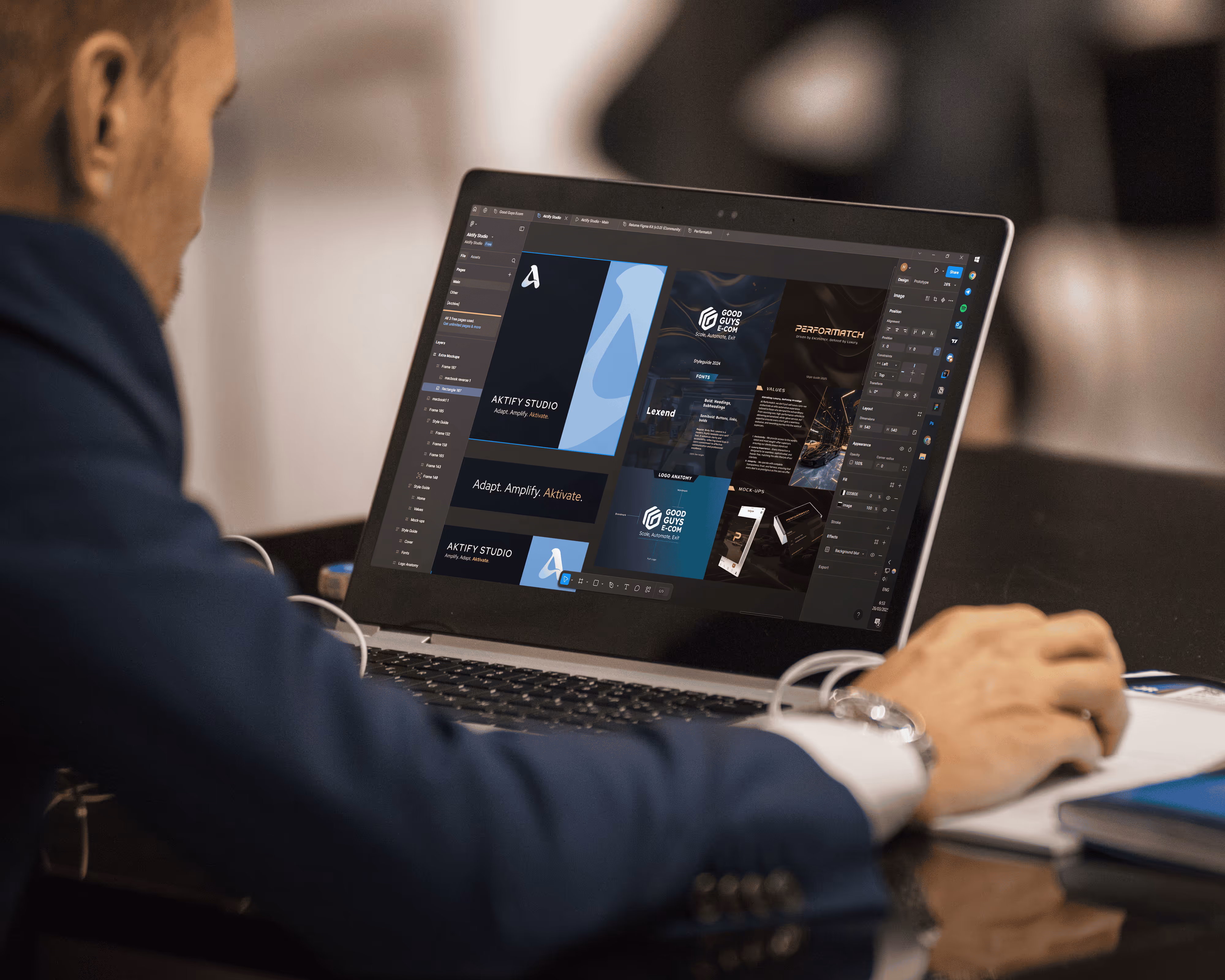 Person in blue jacket working on a laptop displaying a design application with branding and layout elements.