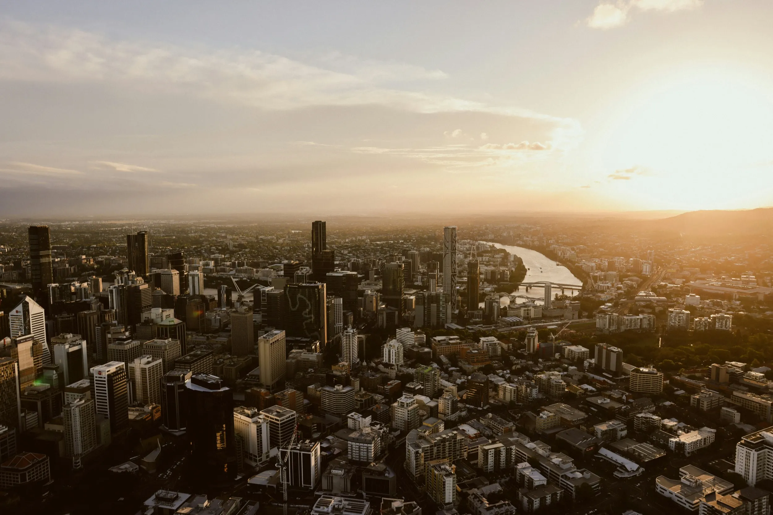 Aerial view of city skyline at sunset with river and tall buildings.