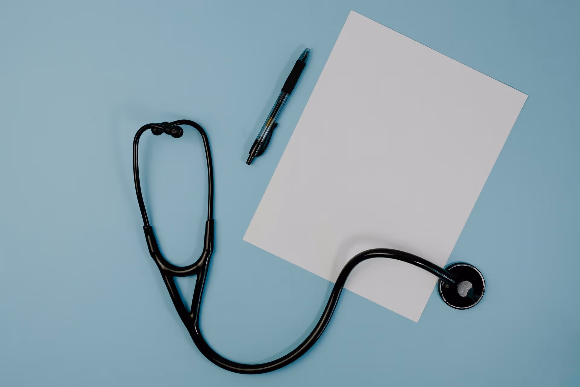 A stethoscope, a blank white sheet, and a pen lie on a light blue background, symbolizing healthcare, medical documentation, and professional tone.