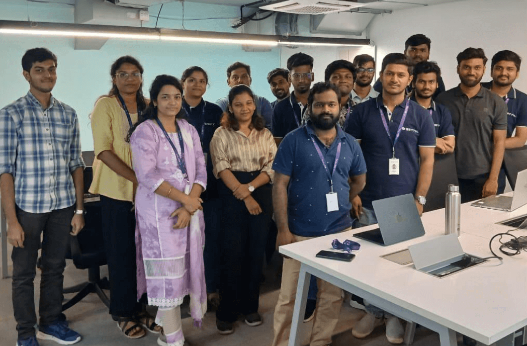 Group of young professionals standing together in a modern office environment with laptops and a water bottle on the table.