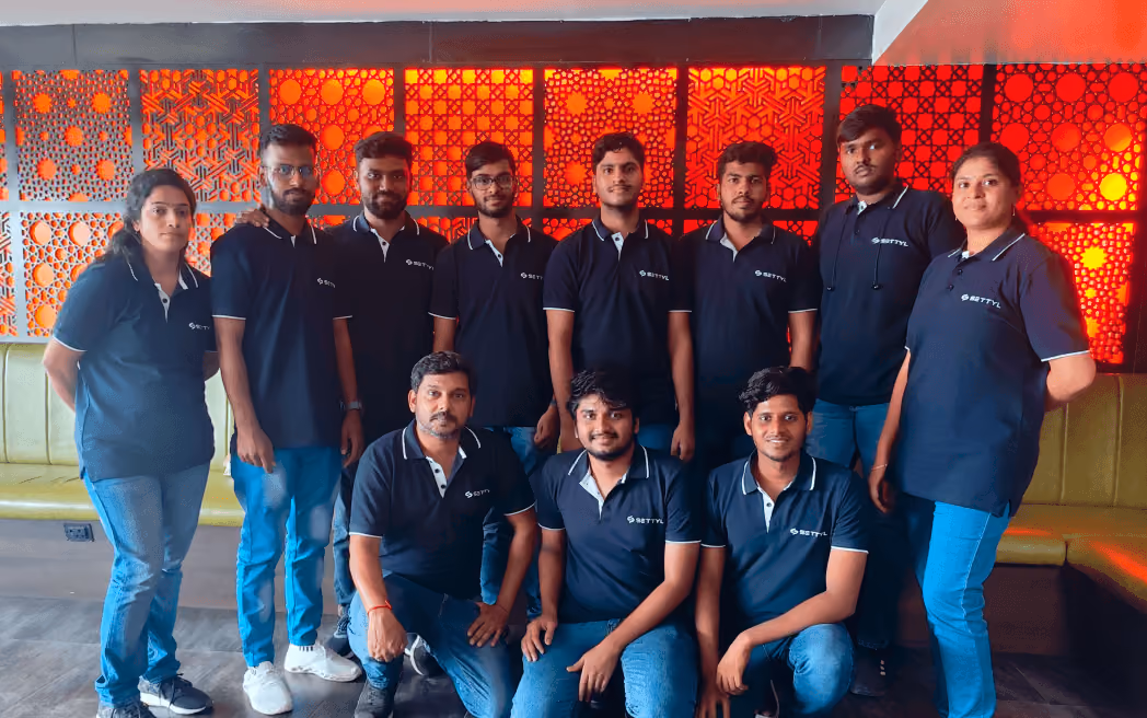 Group of eleven people wearing matching black SETTYL polo shirts posing indoors against a wall with decorative red and orange patterned panels.