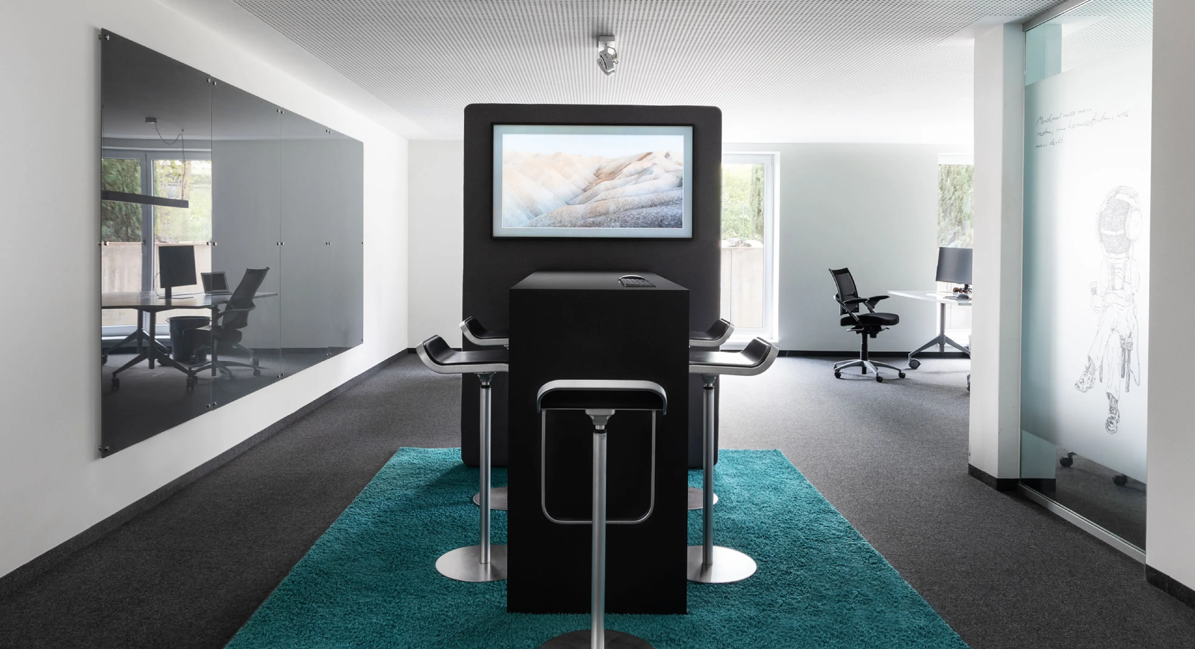 Moderner Besprechungsbereich mit schwarzem hohen Tisch, Barhockern auf blauem Teppich und einem Bildschirm mit Landschaftsfoto.