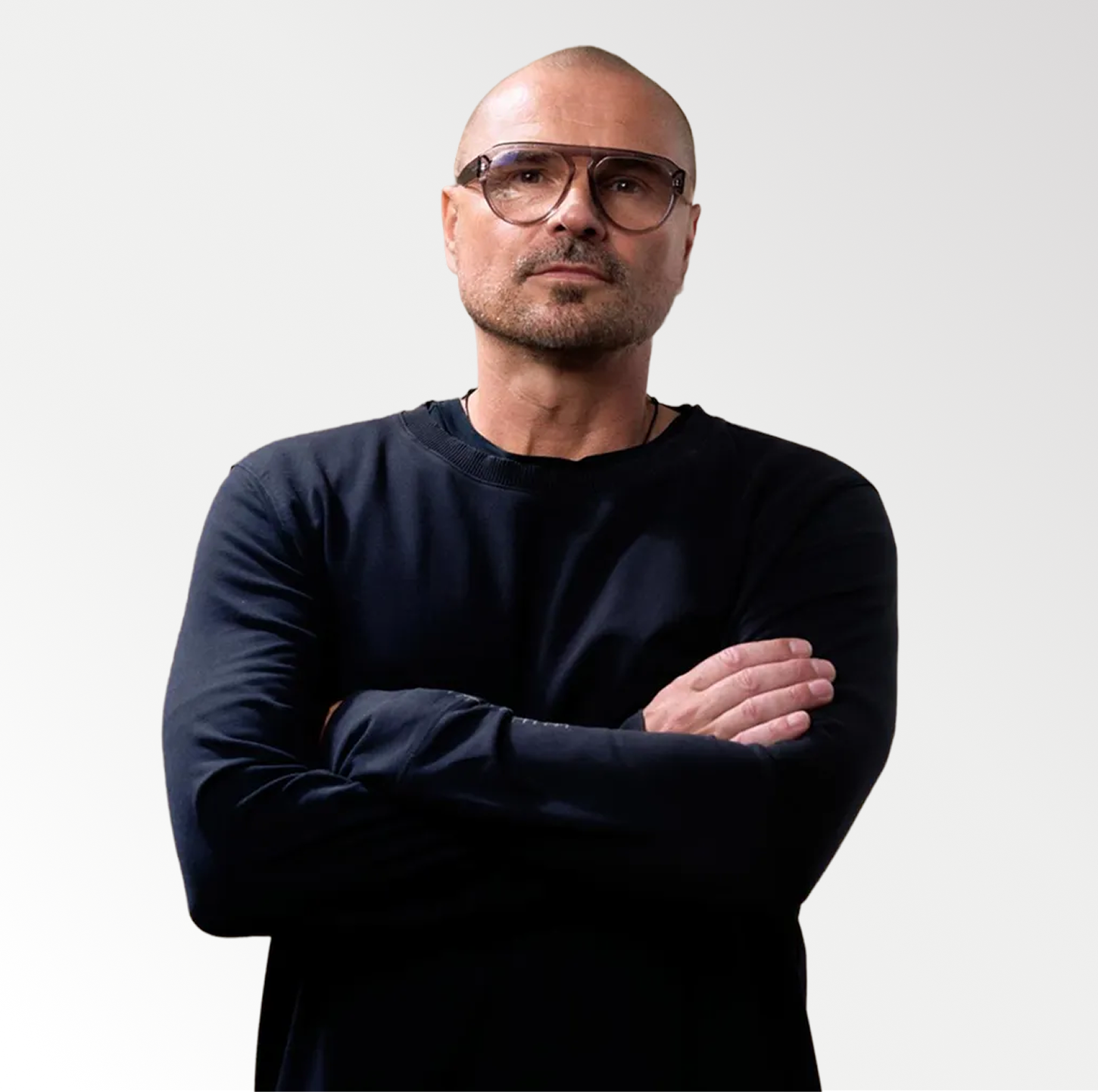 Mann mit Glatze und Brille, der in schwarzem Pullover die Arme verschränkt.
