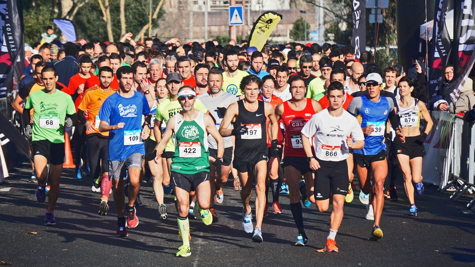 A diverse group of runners competes in a road race, wearing colorful athletic gear. They appear focused and energetic, surrounded by a crowd of spectators.