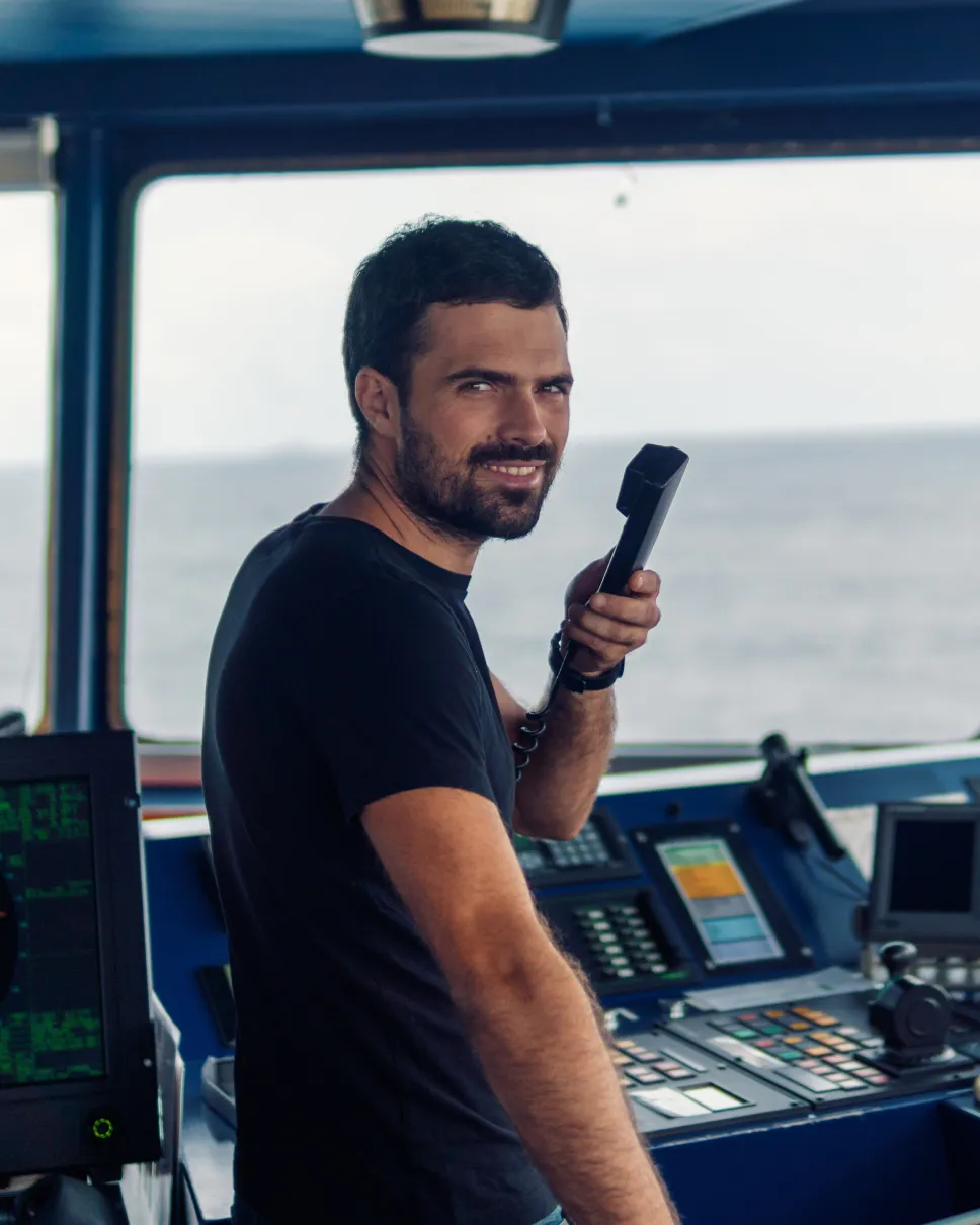 A person in a control room, smiling and looking at the camera
