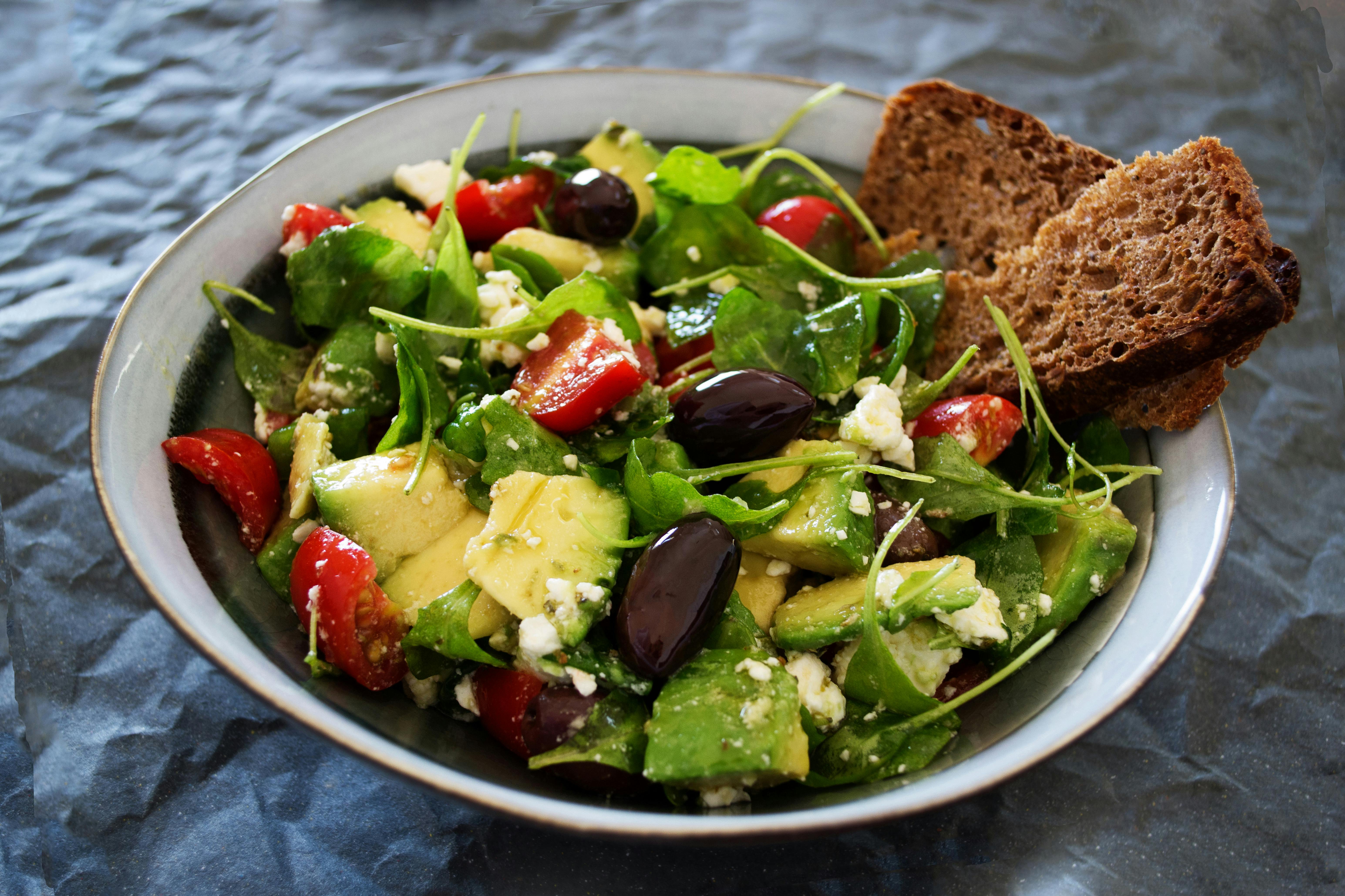 Healthy salad with greens, strawberry, olives, and broccoli while wheat bread slices on the side.