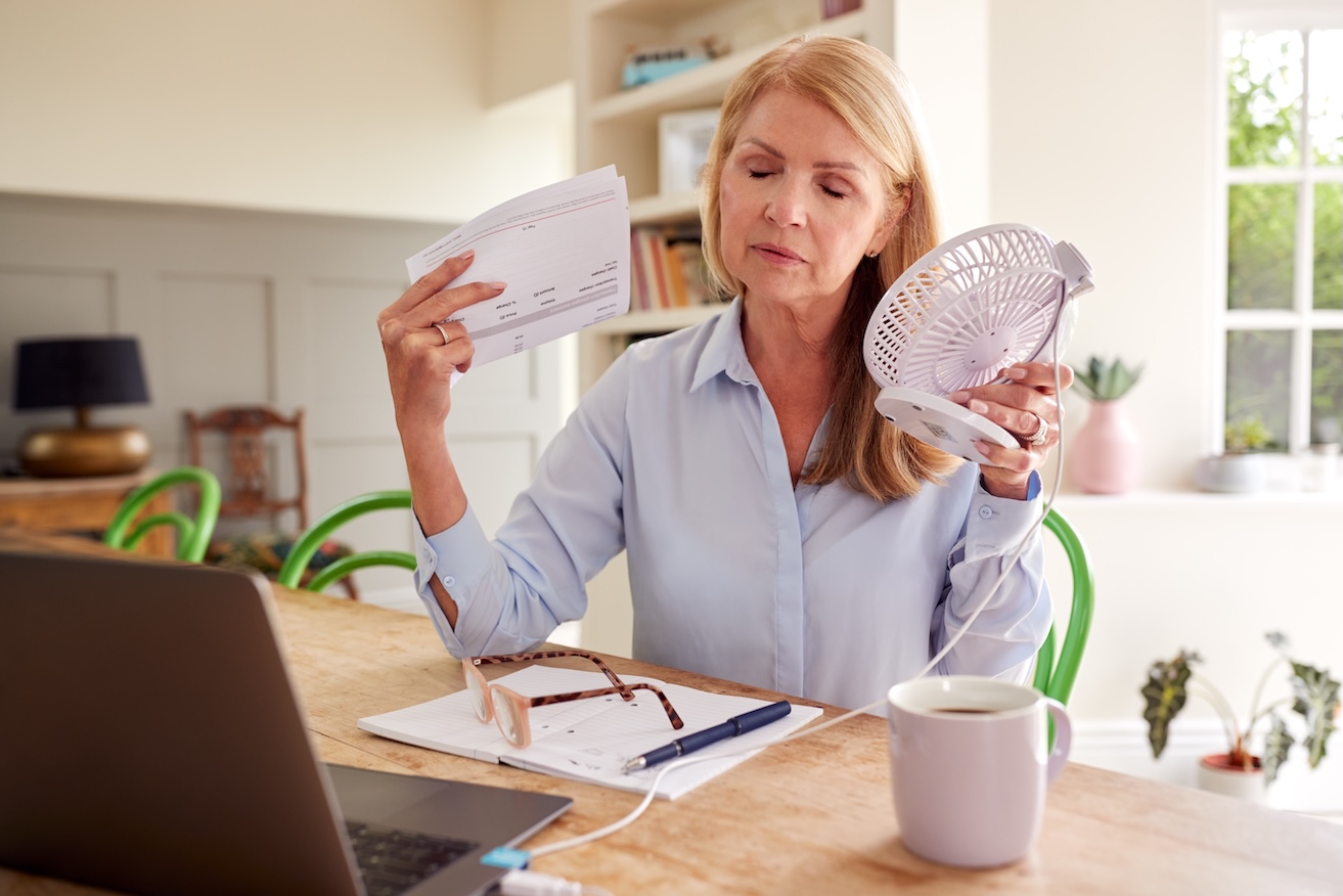 Middle-aged blonde woman having a hot flash and waving a paper and fan in front of her face