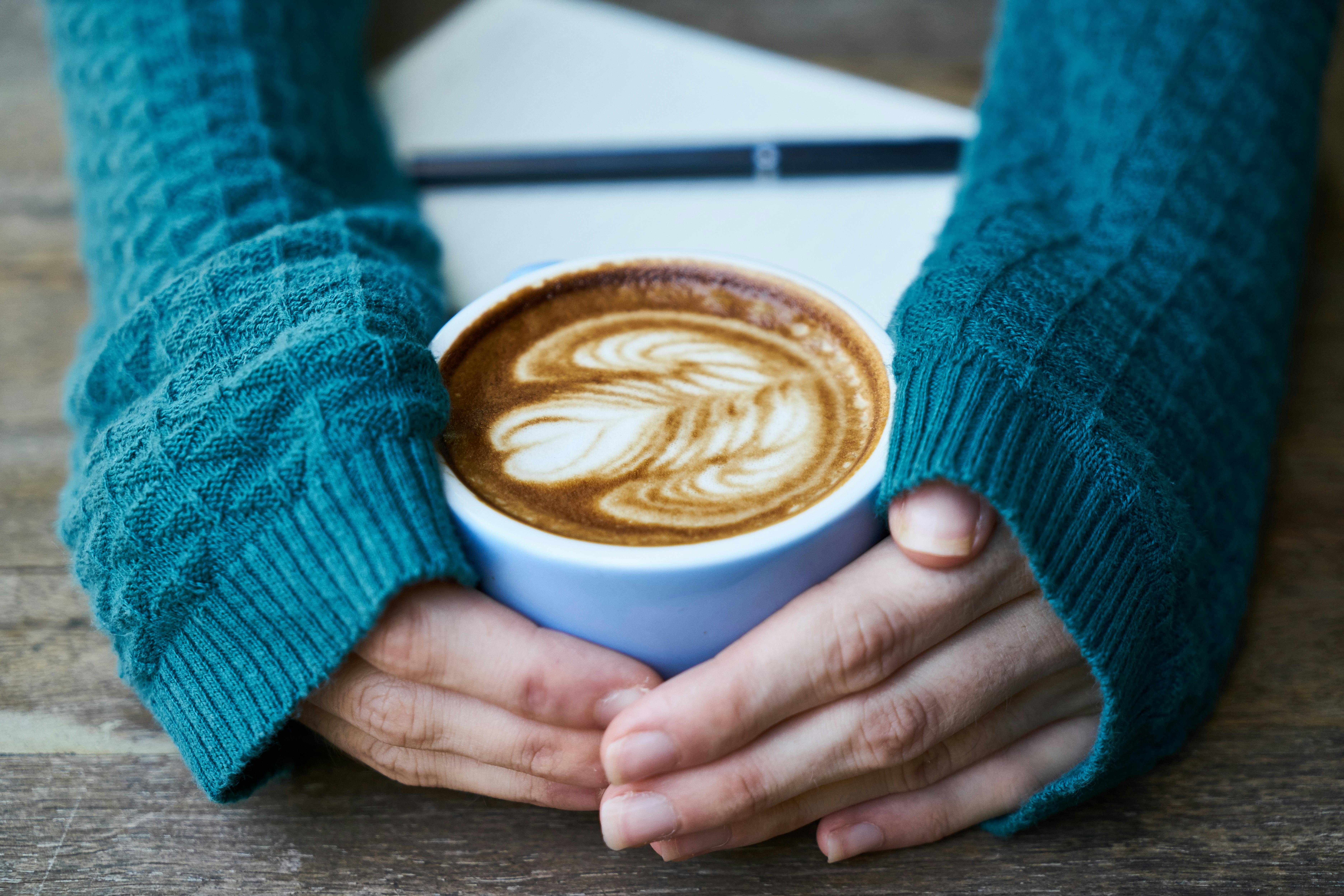 Arms in a teal sweater wrap around a mug of coffee