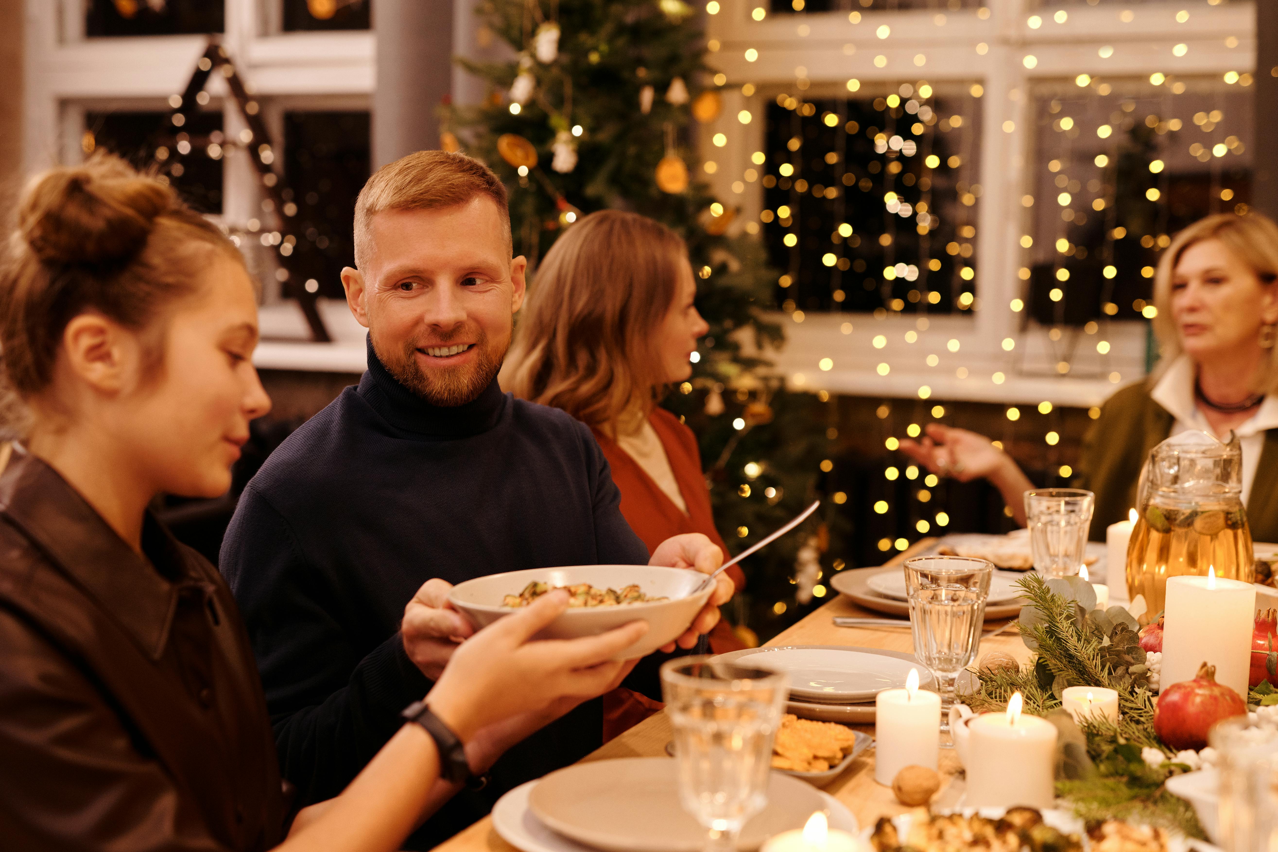 Man passes bowl of food to young woman during a holiday dinner party