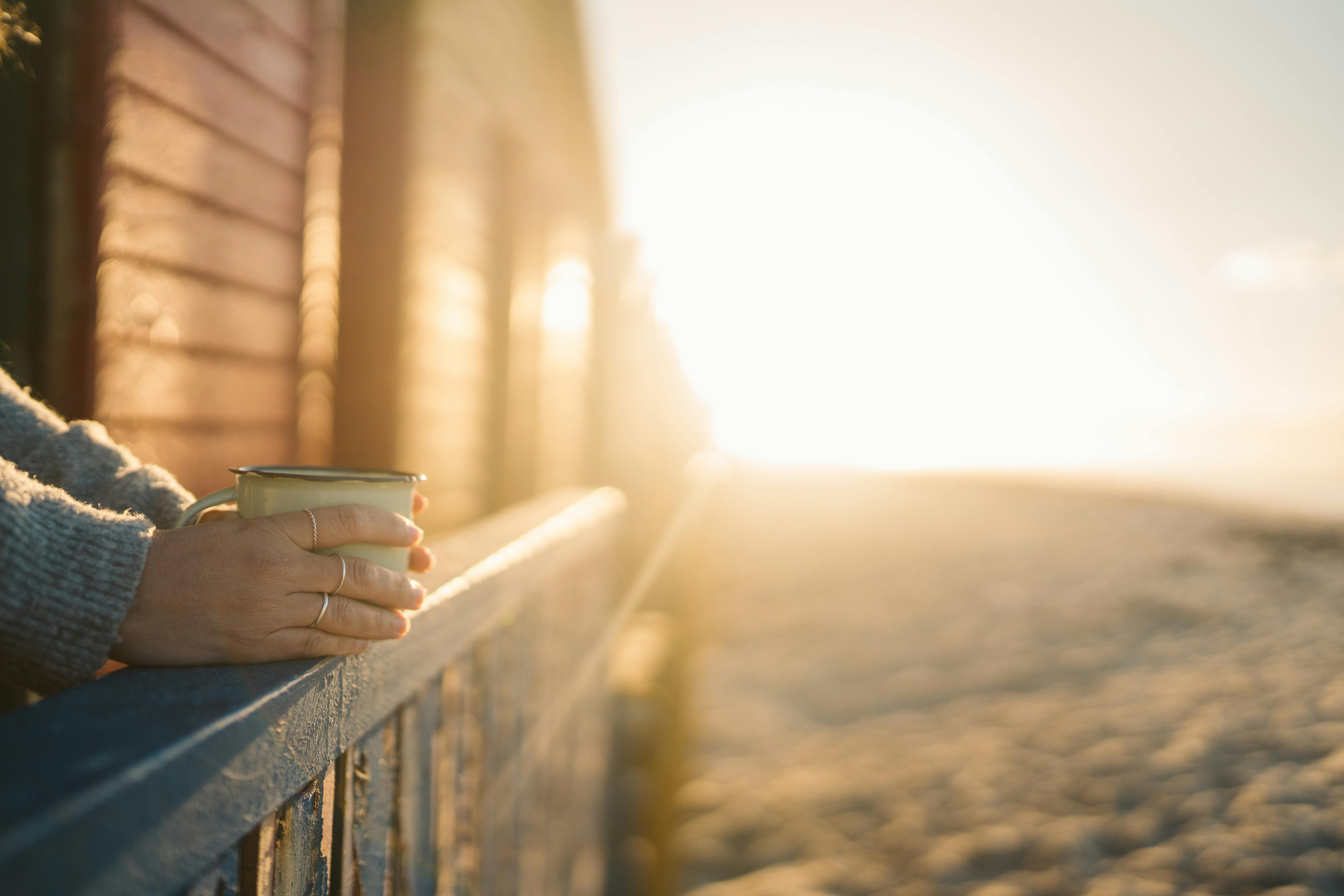 Person's hands around coffee mug with sunrise in the background