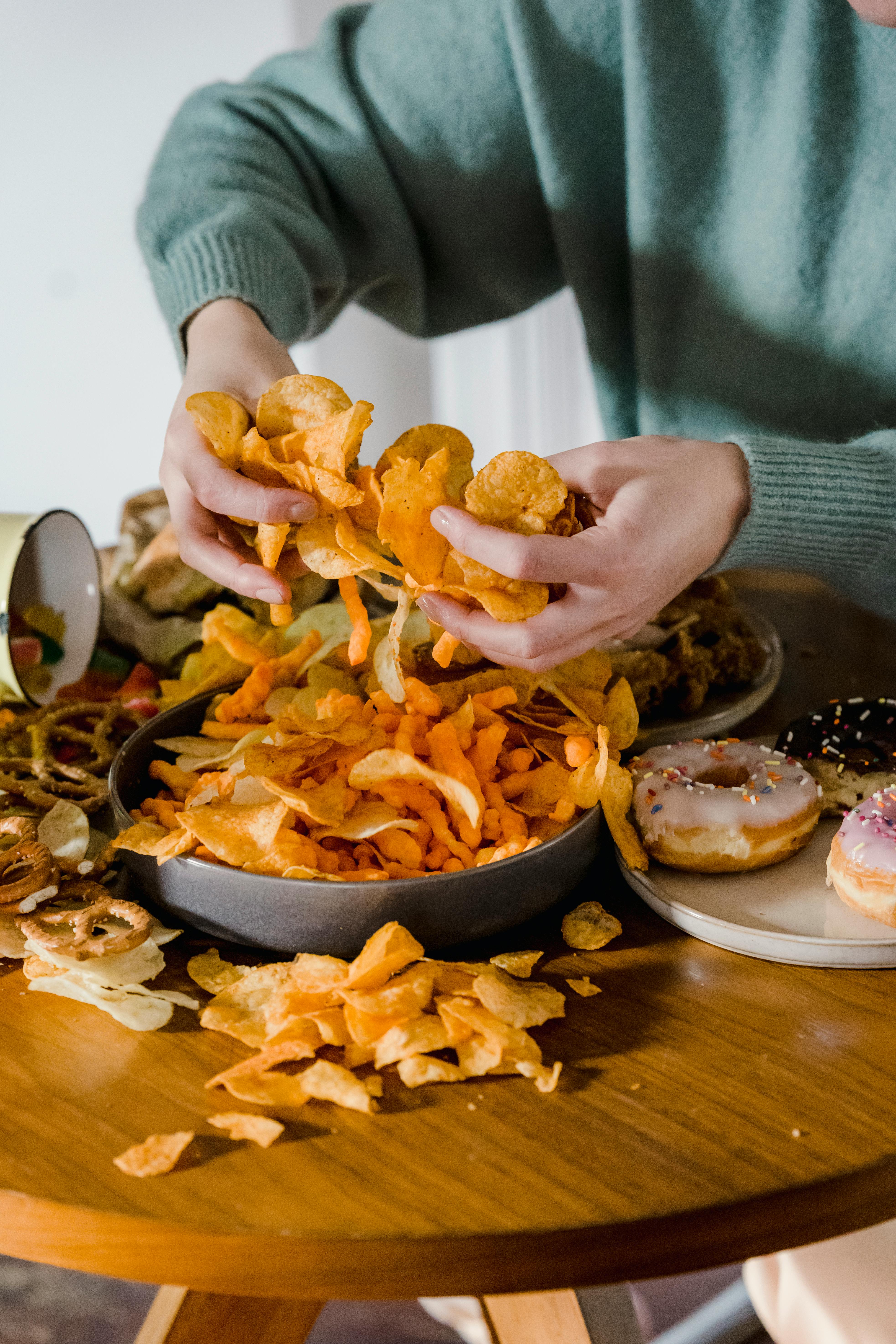 Person with hands full of chips, with more chips and donuts on the table