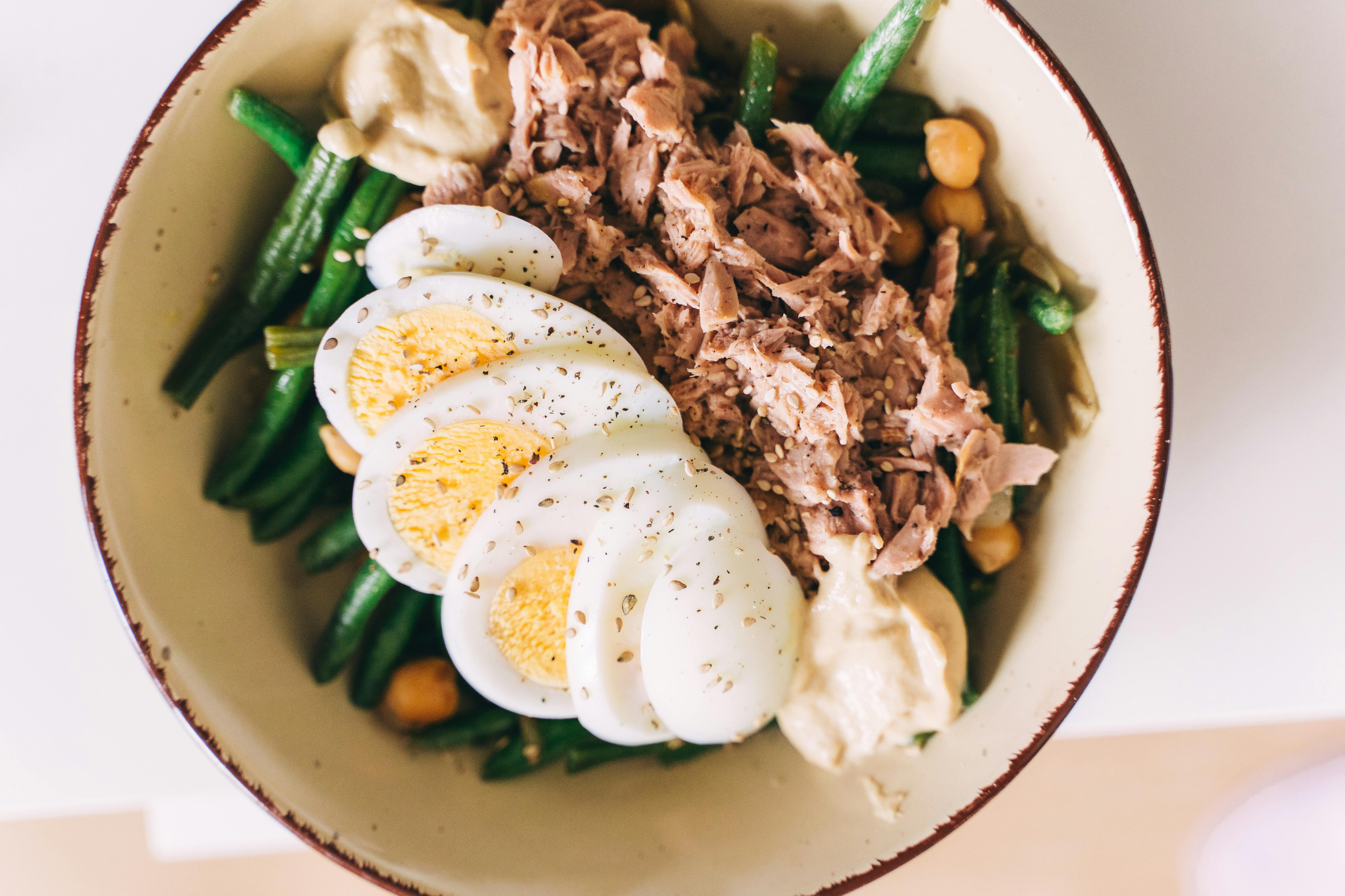 Bowl of food containing green beans, hard-boiled eggs, and shredded chicken