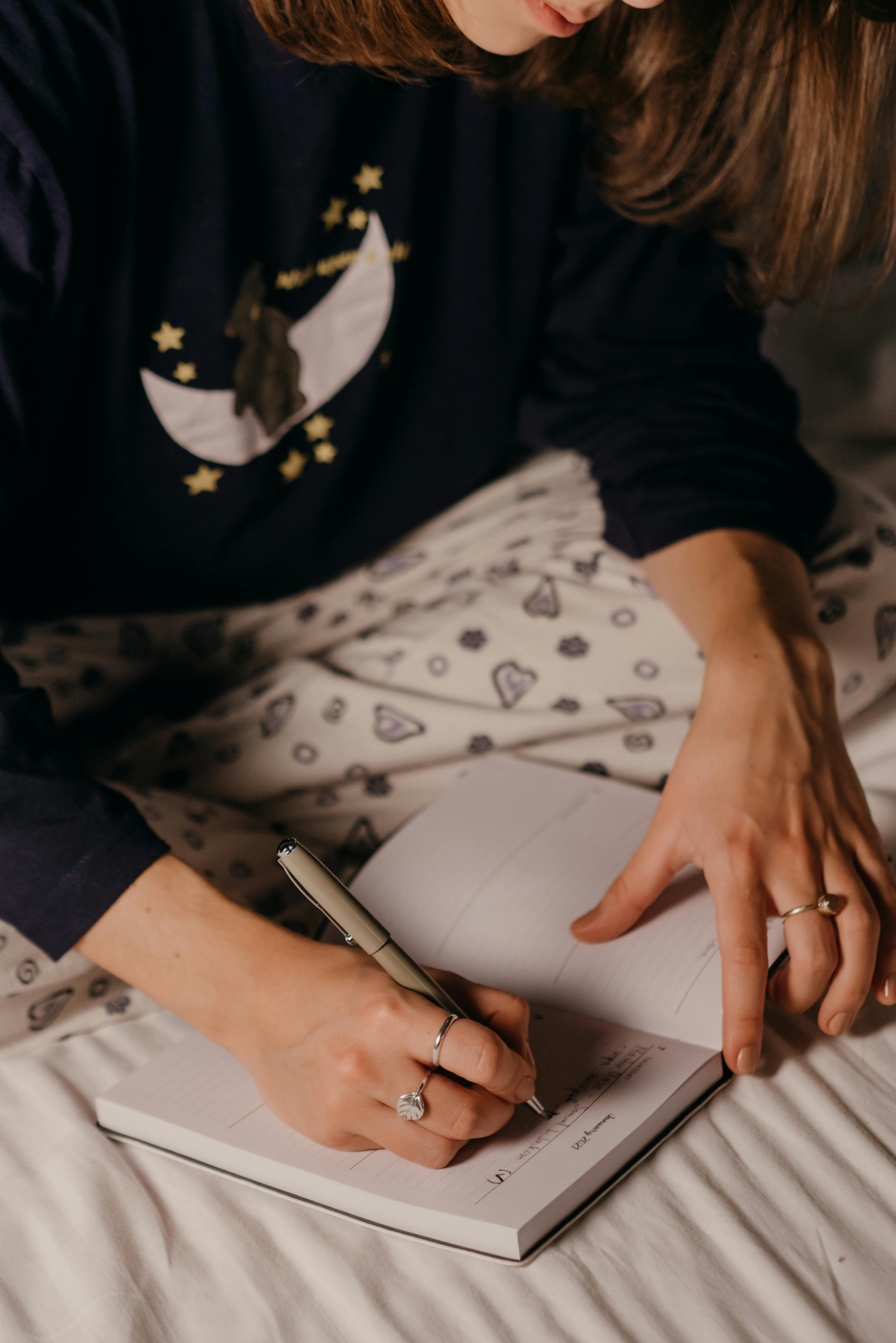 Young woman in pajamas writing in planner in bed