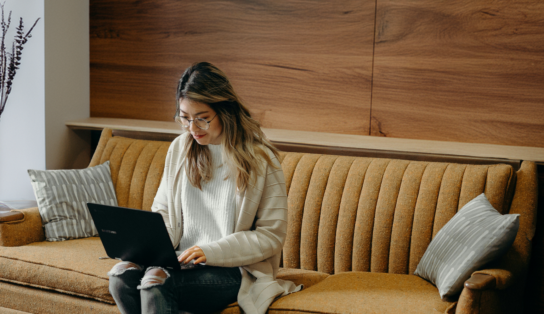 Young woman sitting on couch working on laptop