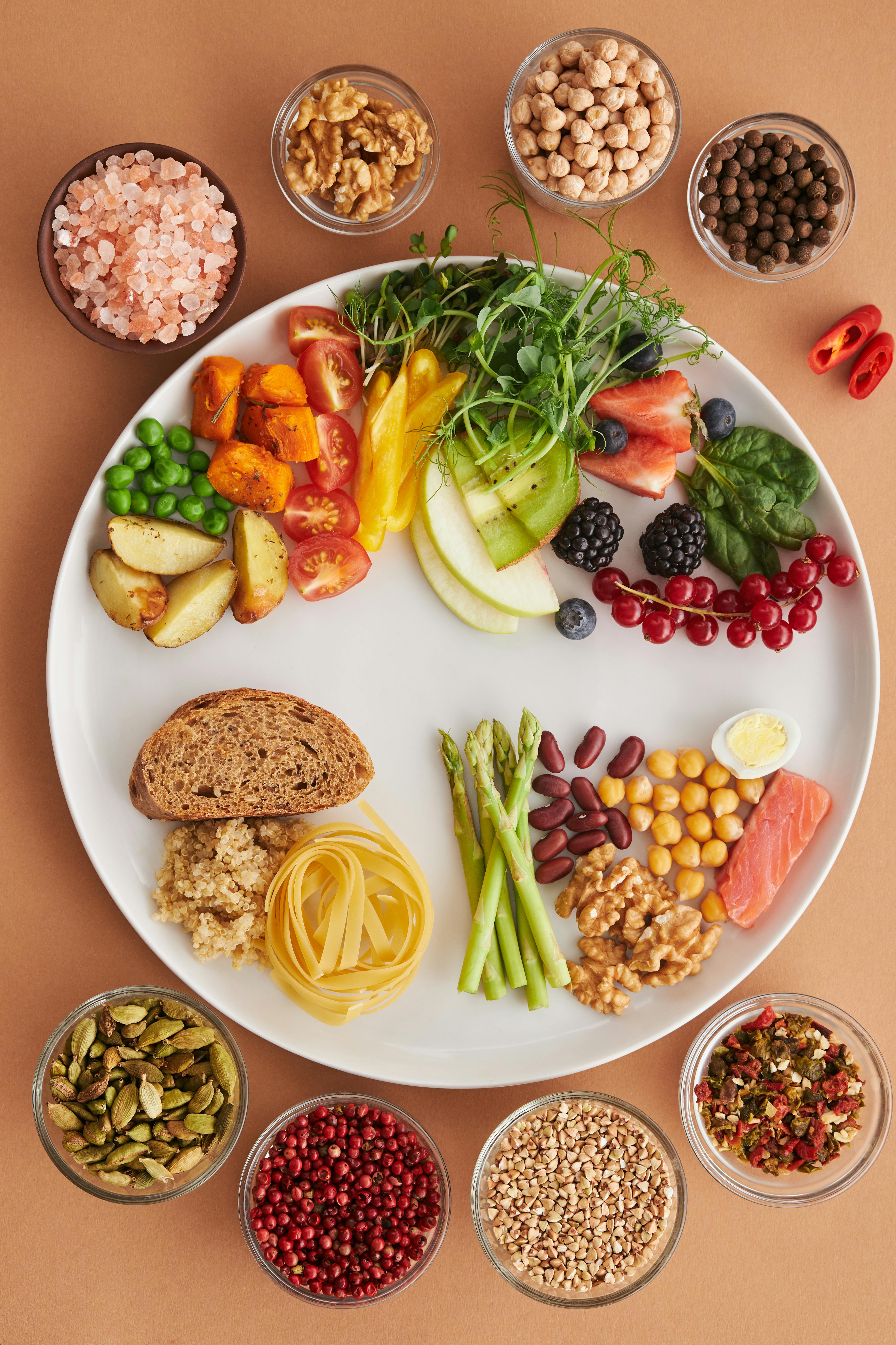 Plate full of fruits, vegetables, and whole grains surrounded by small bowls of nuts, seeds, and legumes