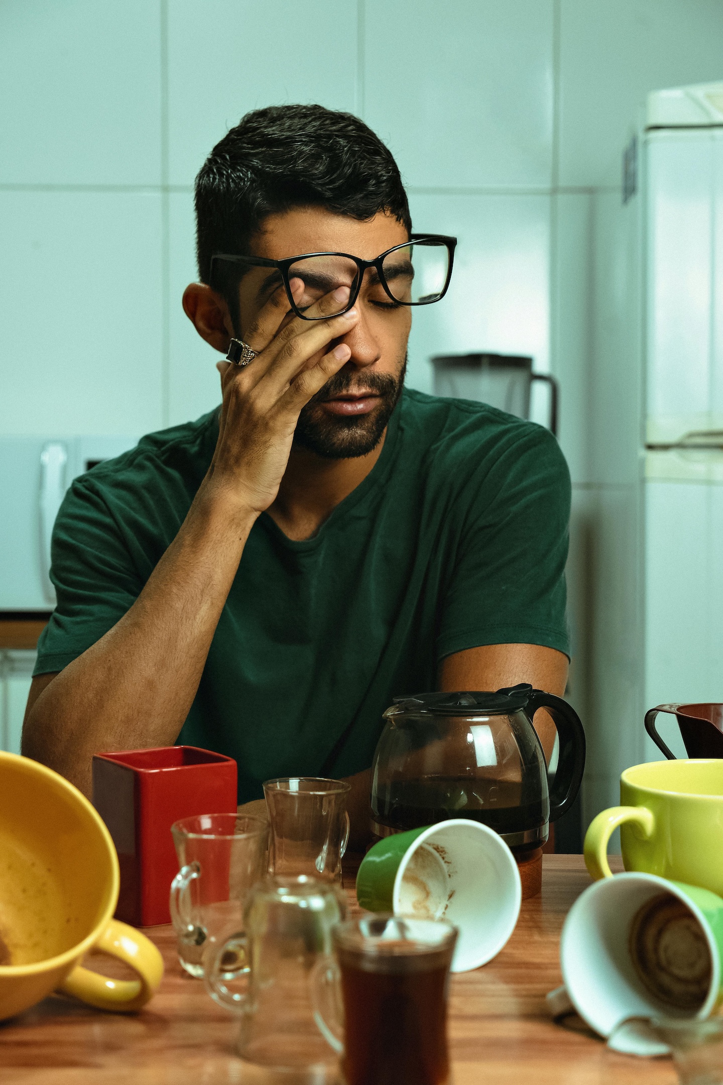 Man rubbing his eyes in front of empty coffee cups